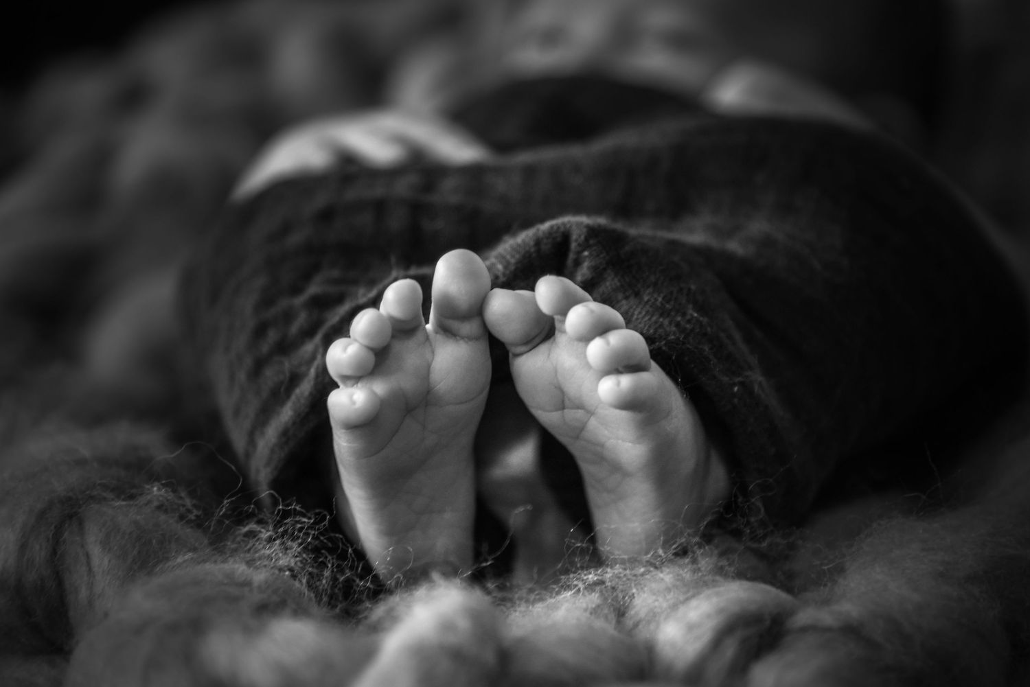 Black and white close-up photograph of tiny baby feet in soft focus against dark background.