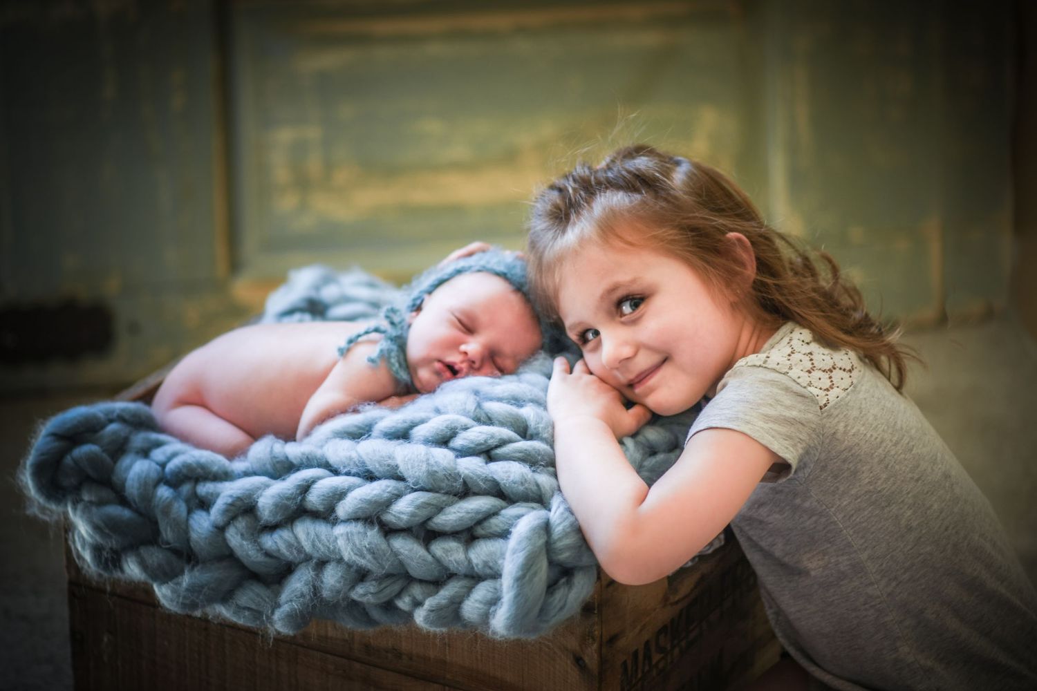 A baby sleeps peacefully under a soft blue blanket while being watched over.