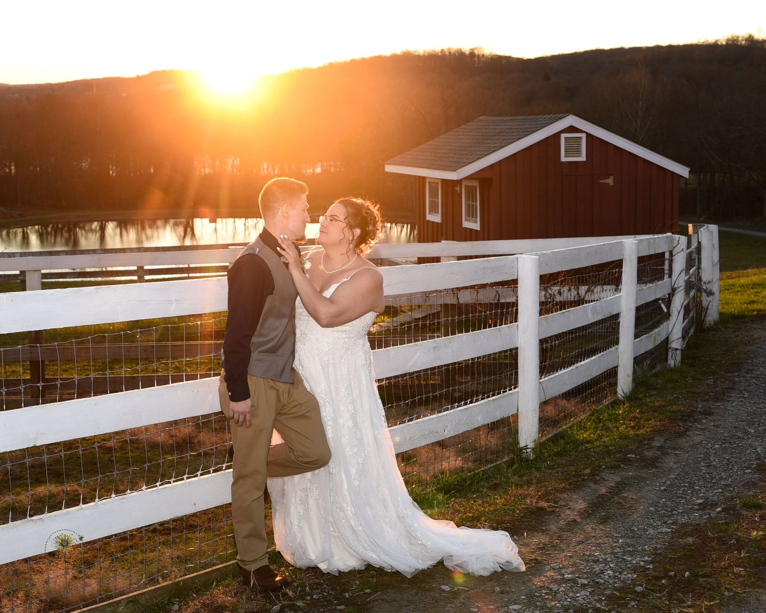 Sunset wedding portraits by a white fence at a rustic farm venue.
