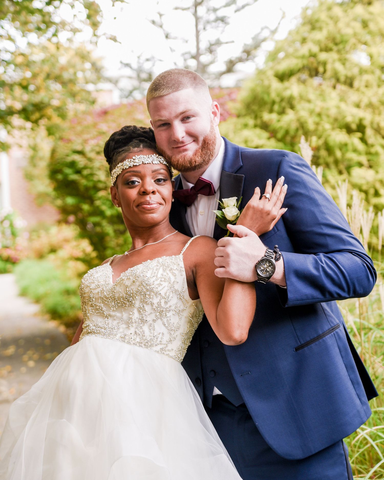 Joyful wedding couple embraces and laughs together in an outdoor garden setting.