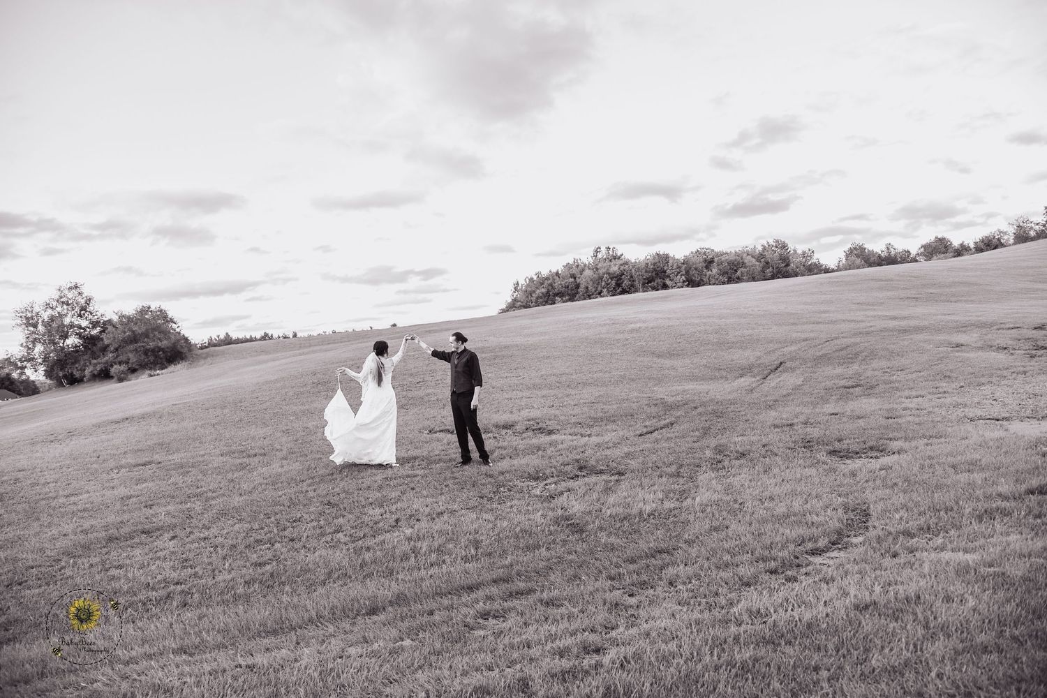 Black and white landscape photo of a couple walking together across a rolling hillside.