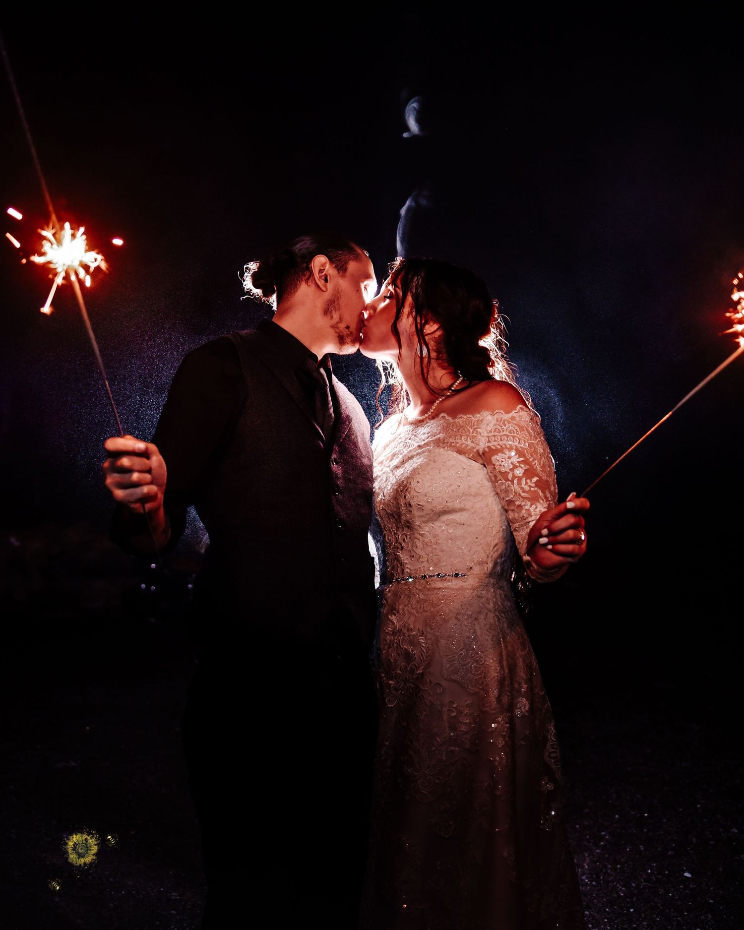 Newlyweds share an intimate moment while holding sparklers against a dark night sky.