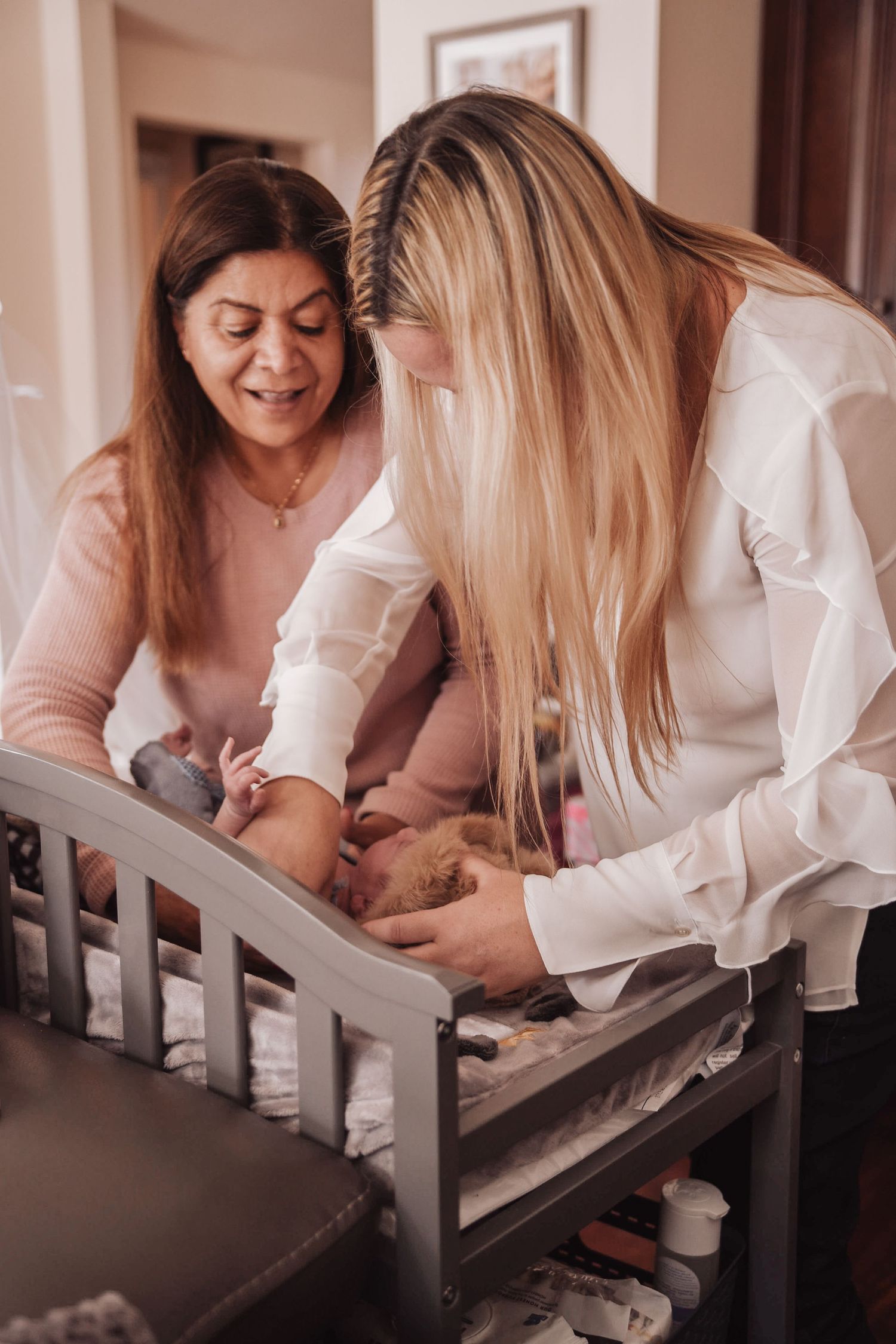 Multiple images show people leaning over a white crib and interacting with a baby in a warm, intimate setting.