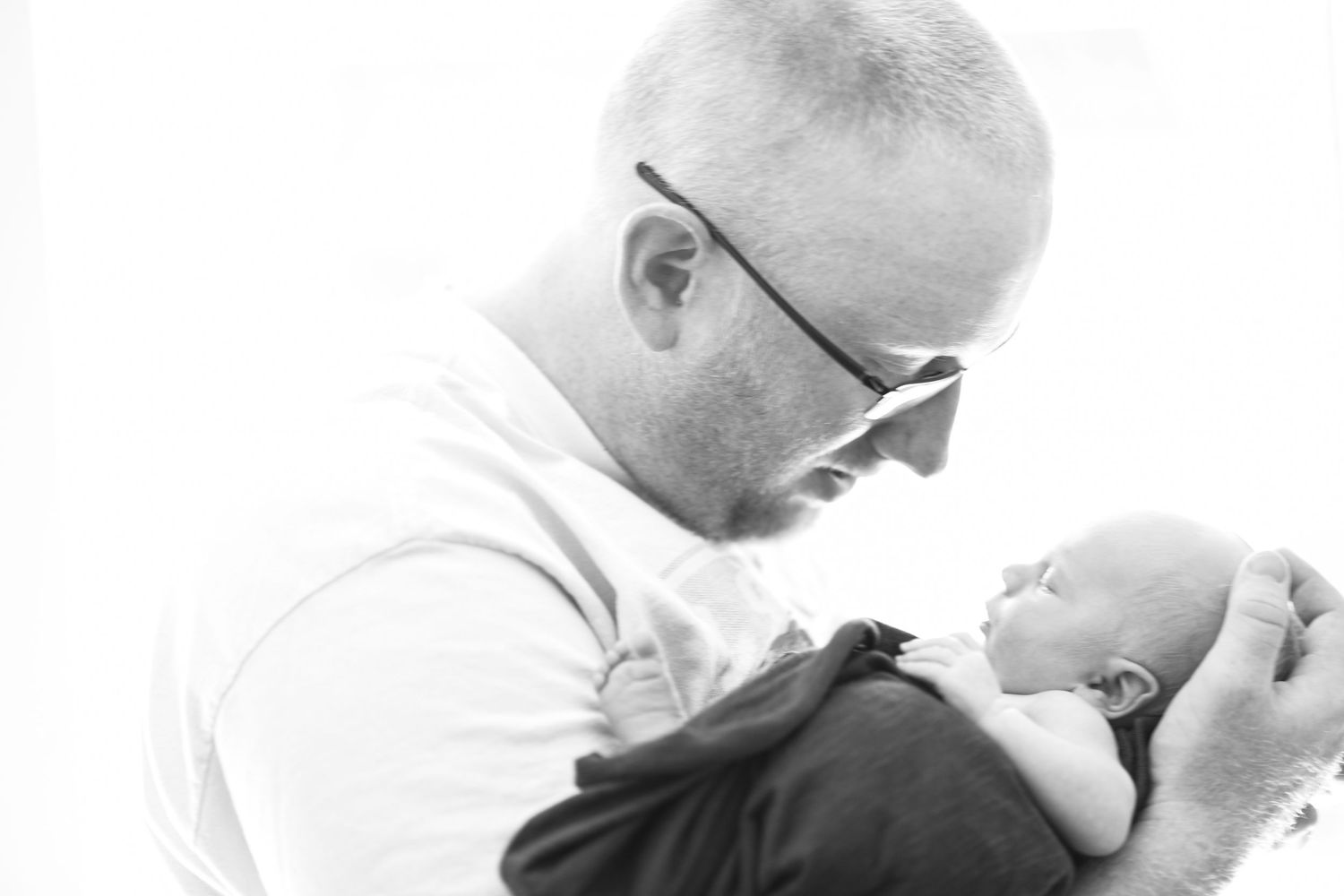 A tender black and white photograph captures an intimate moment between parent and baby in a hospital setting.
