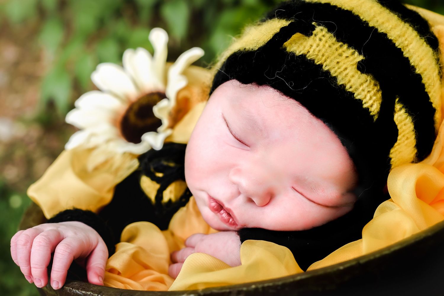A sleeping baby wearing a black and yellow striped bumblebee outfit lying on soft yellow fabric.