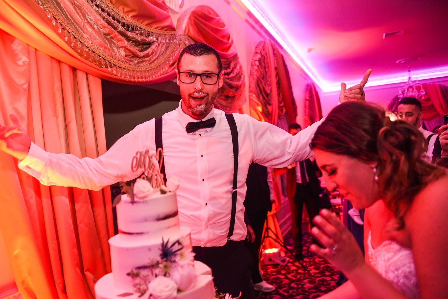 Wedding celebration moment with cake cutting in vibrant pink lighting.