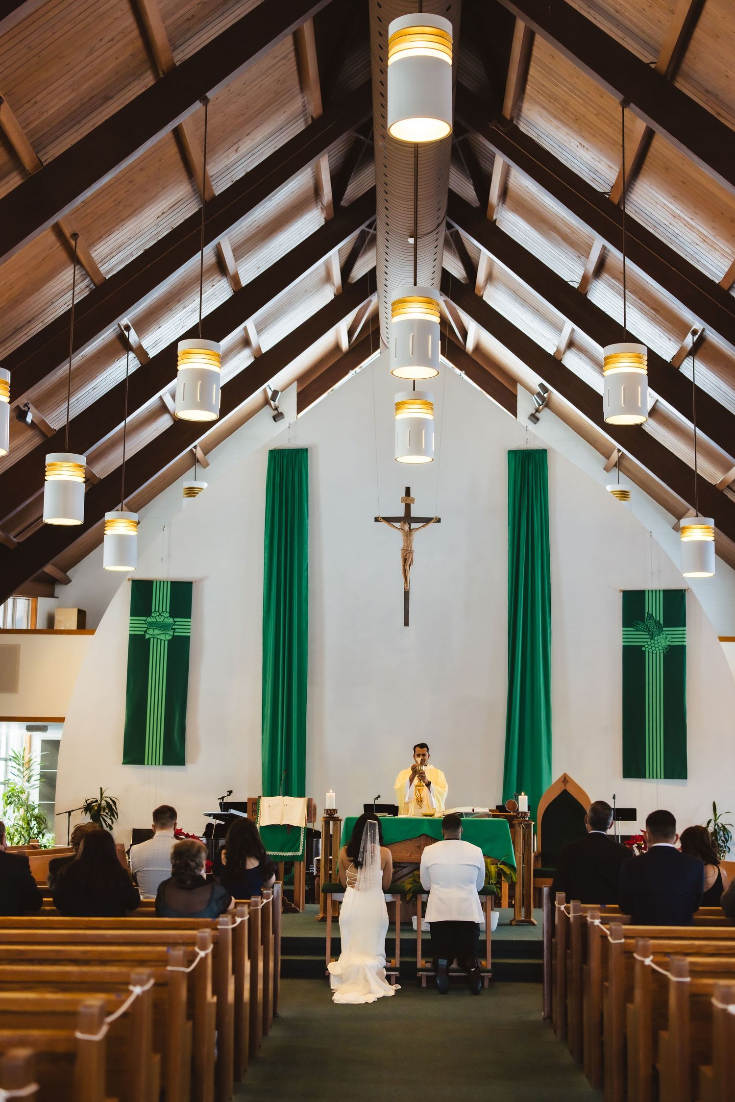 Interior of Catholic church with vaulted ceiling, hanging lights and green banners during ceremony.