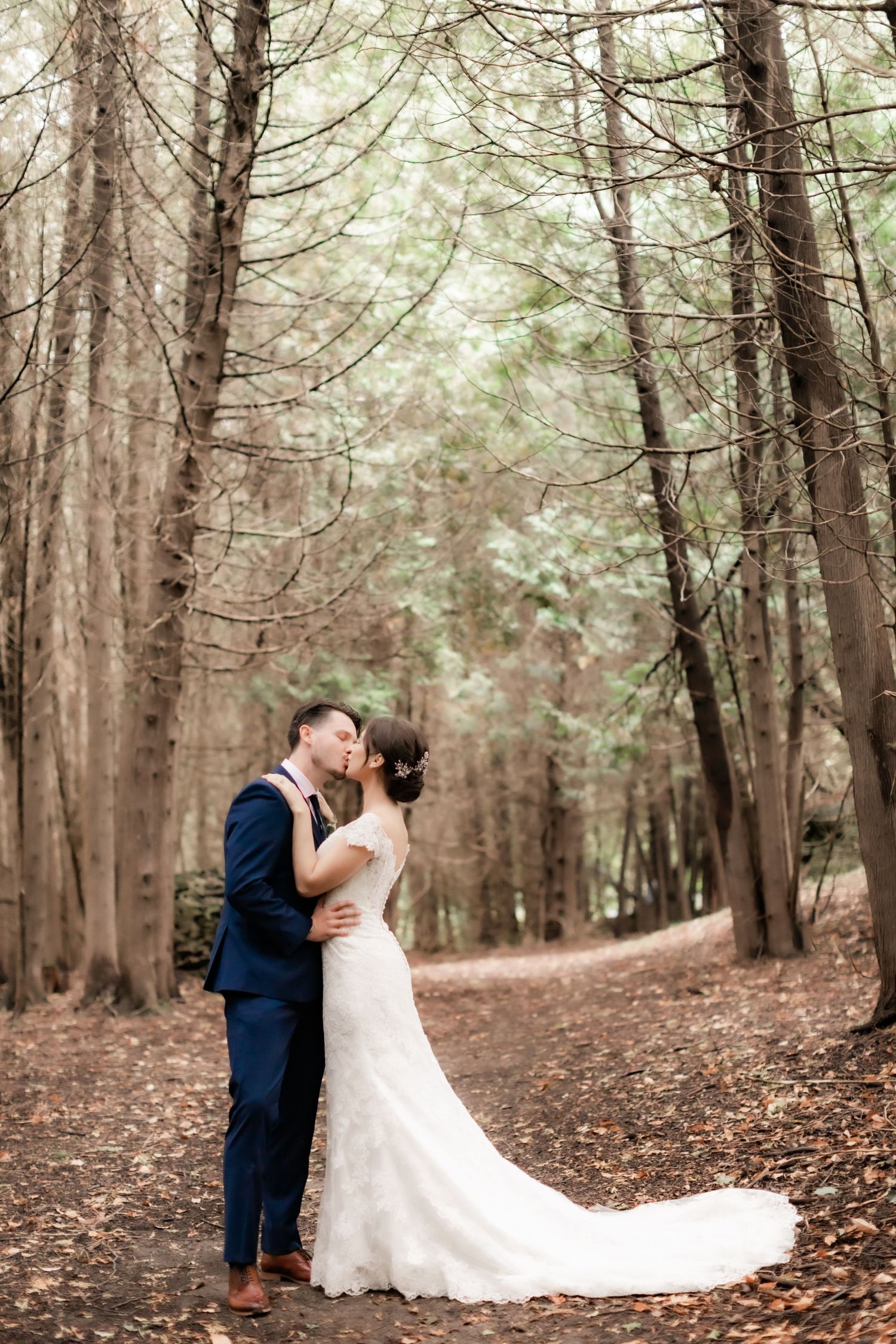 Intimate embrace between newlyweds on leaf-covered forest path.