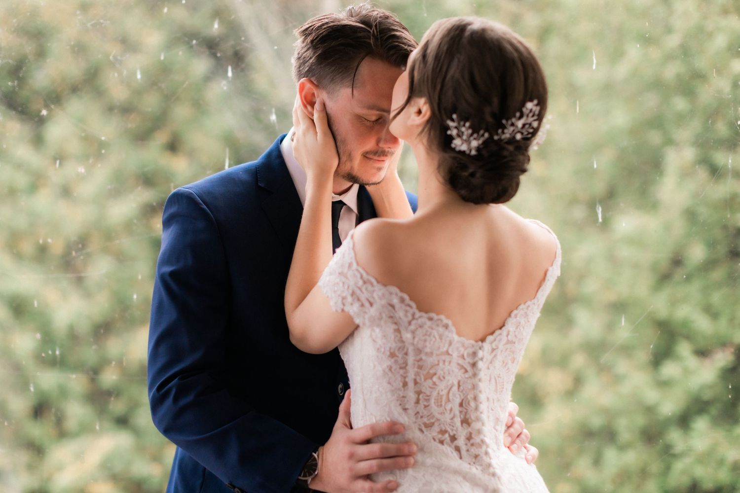 A tender moment between newlyweds with soft rain falling in a garden setting.