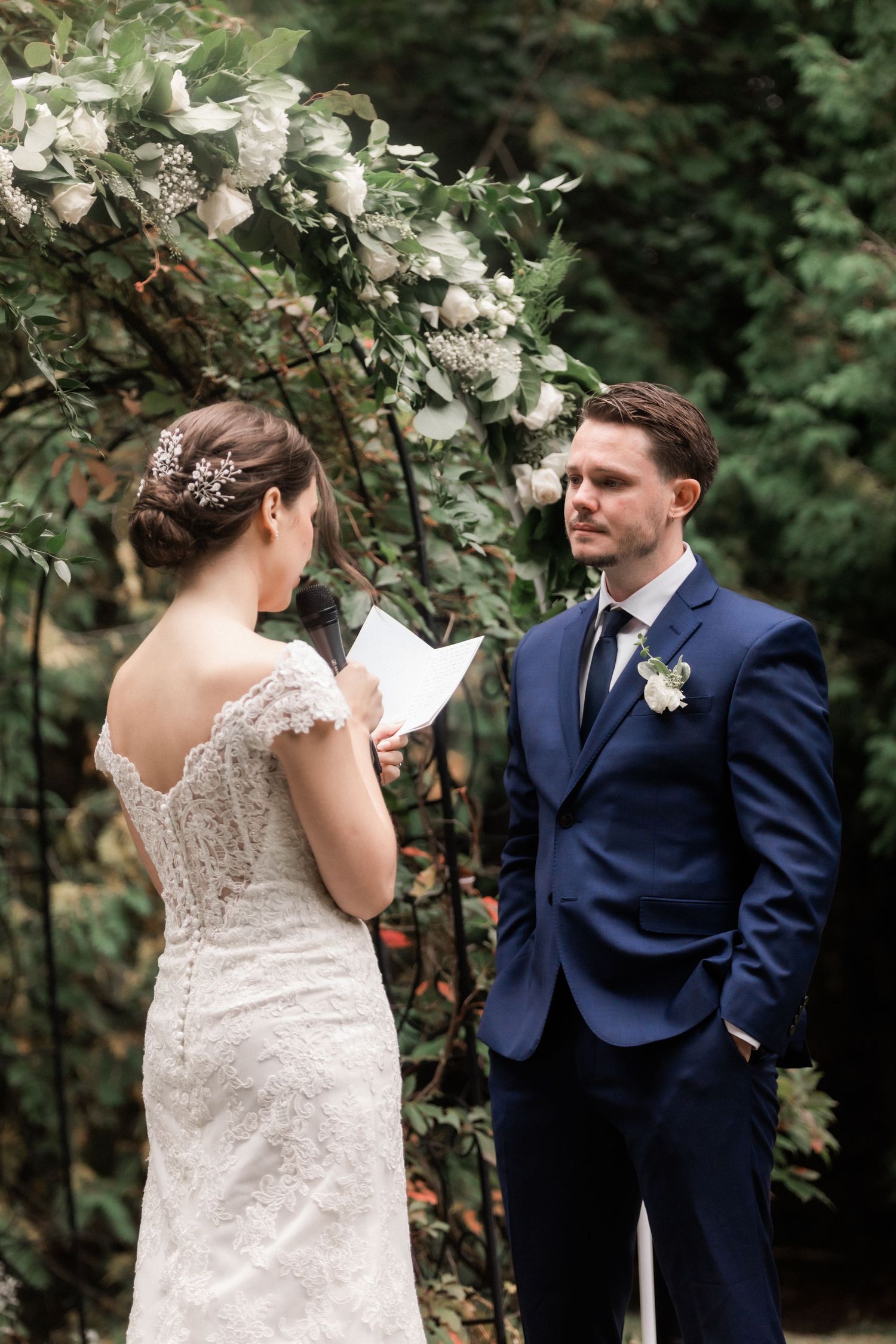 A couple exchanging personal vows beneath a floral arch during their outdoor wedding ceremony.