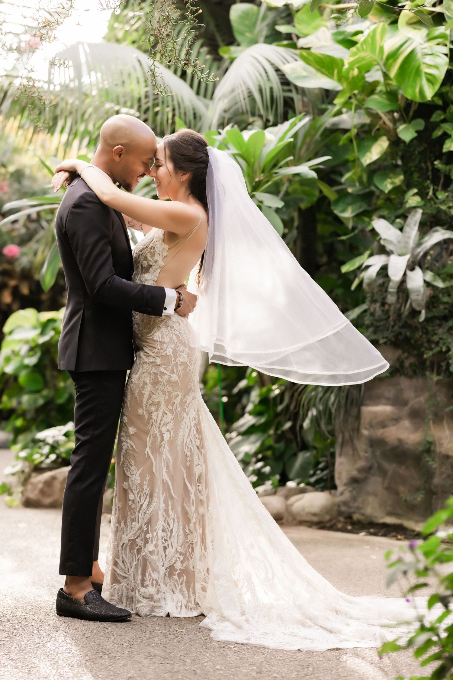 Newlyweds share an intimate embrace surrounded by tropical foliage and greenery.