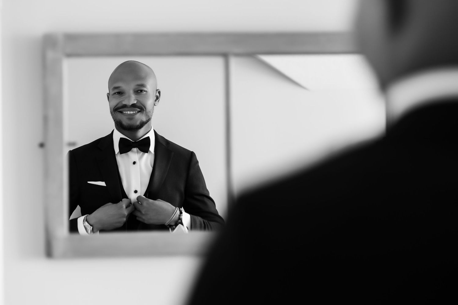 Black and white mirror shot captures person in tuxedo adjusting formal attire.