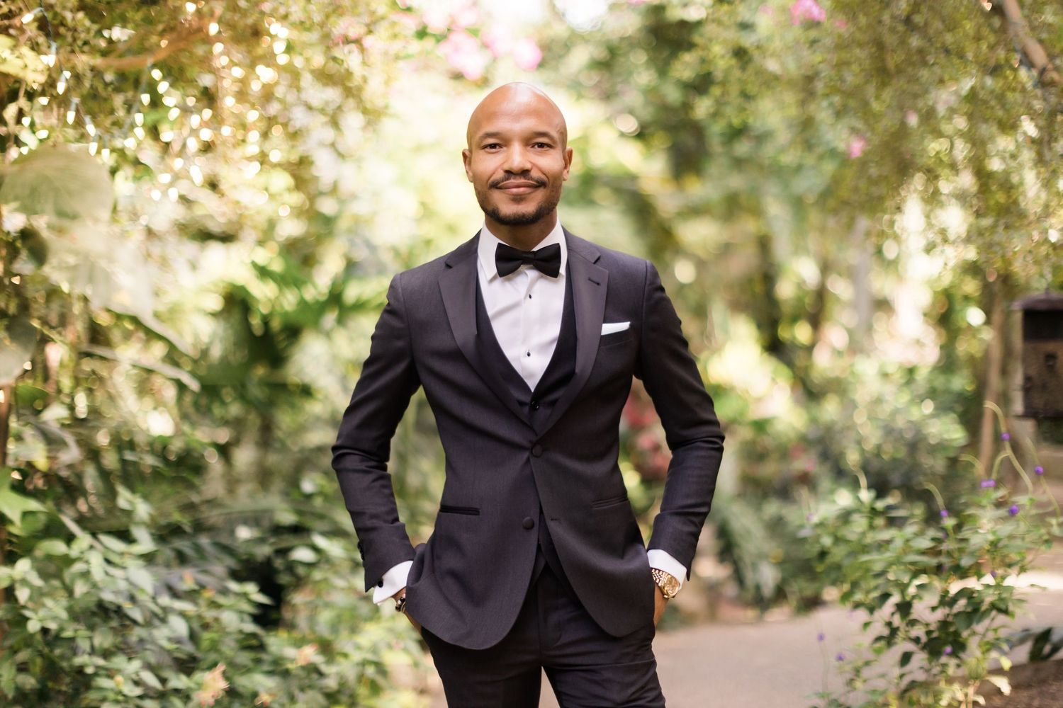 Formal portrait in a lush garden setting with flowering plants and natural light.