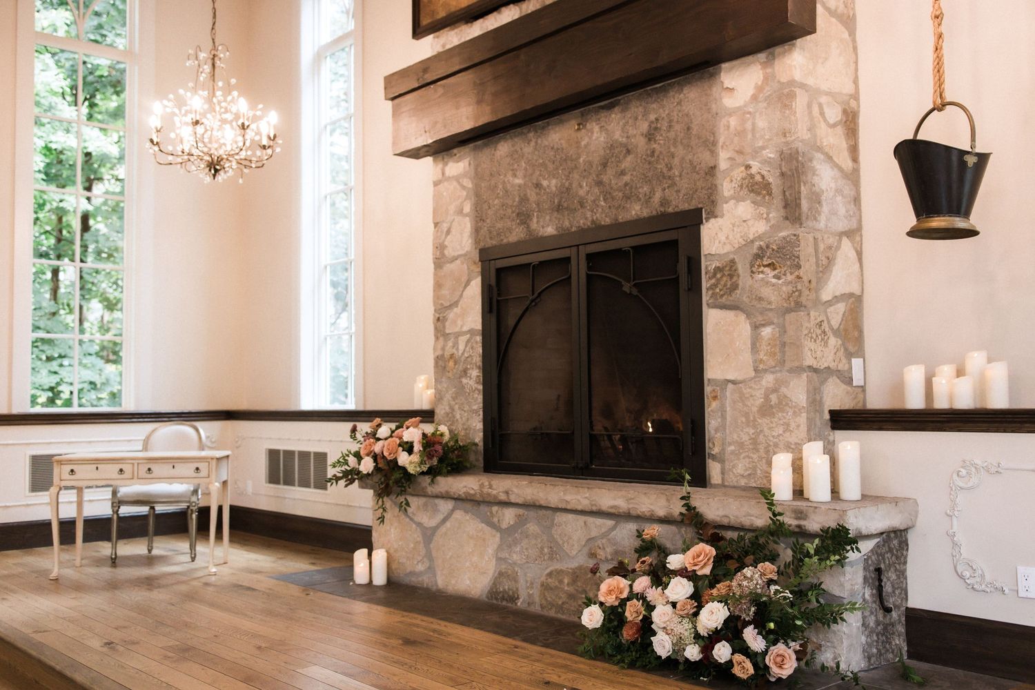 Rustic stone fireplace with floral arrangements and candles in an elegant reception space.