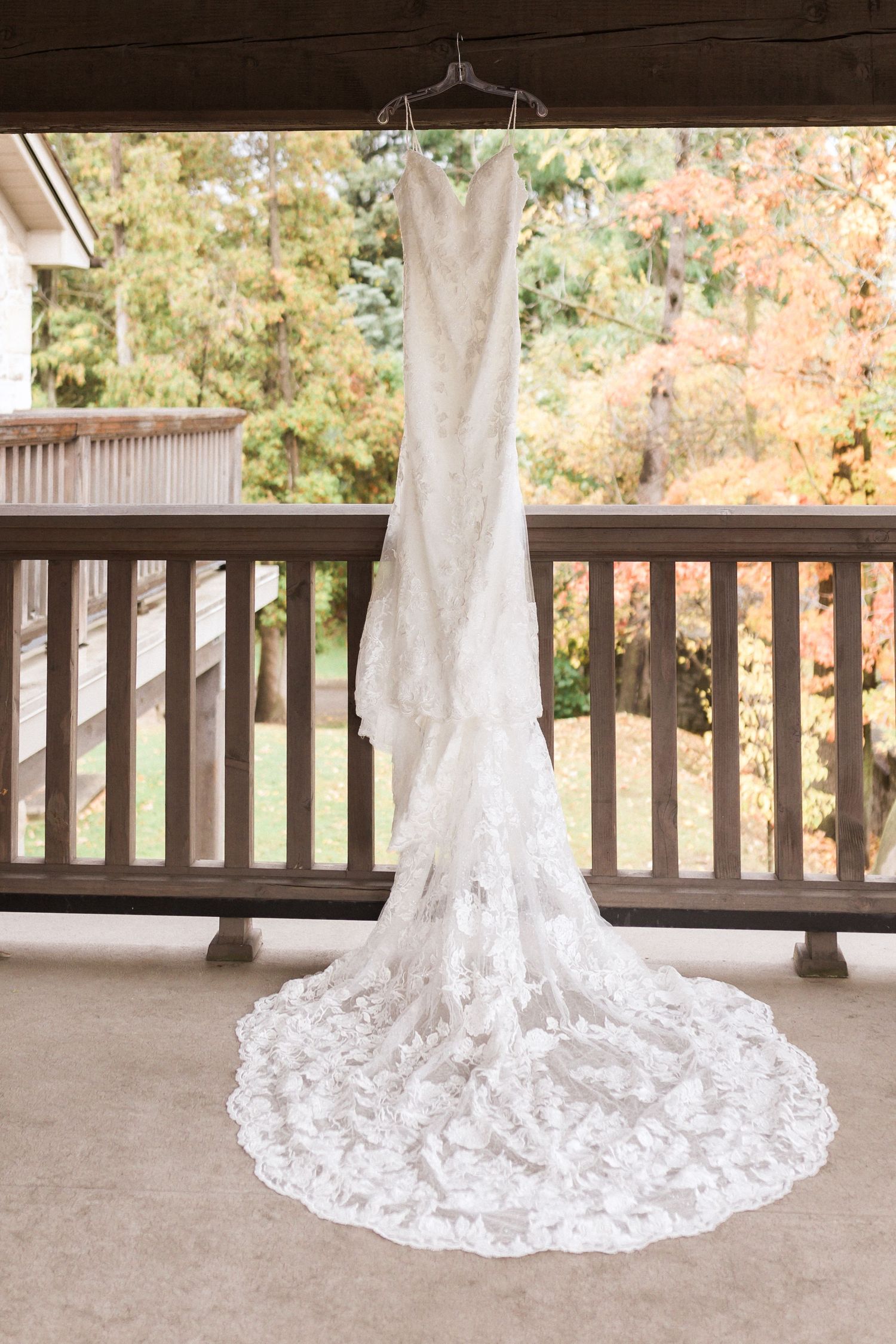 Elegant white lace wedding dress with long train hanging on display on outdoor porch railing.