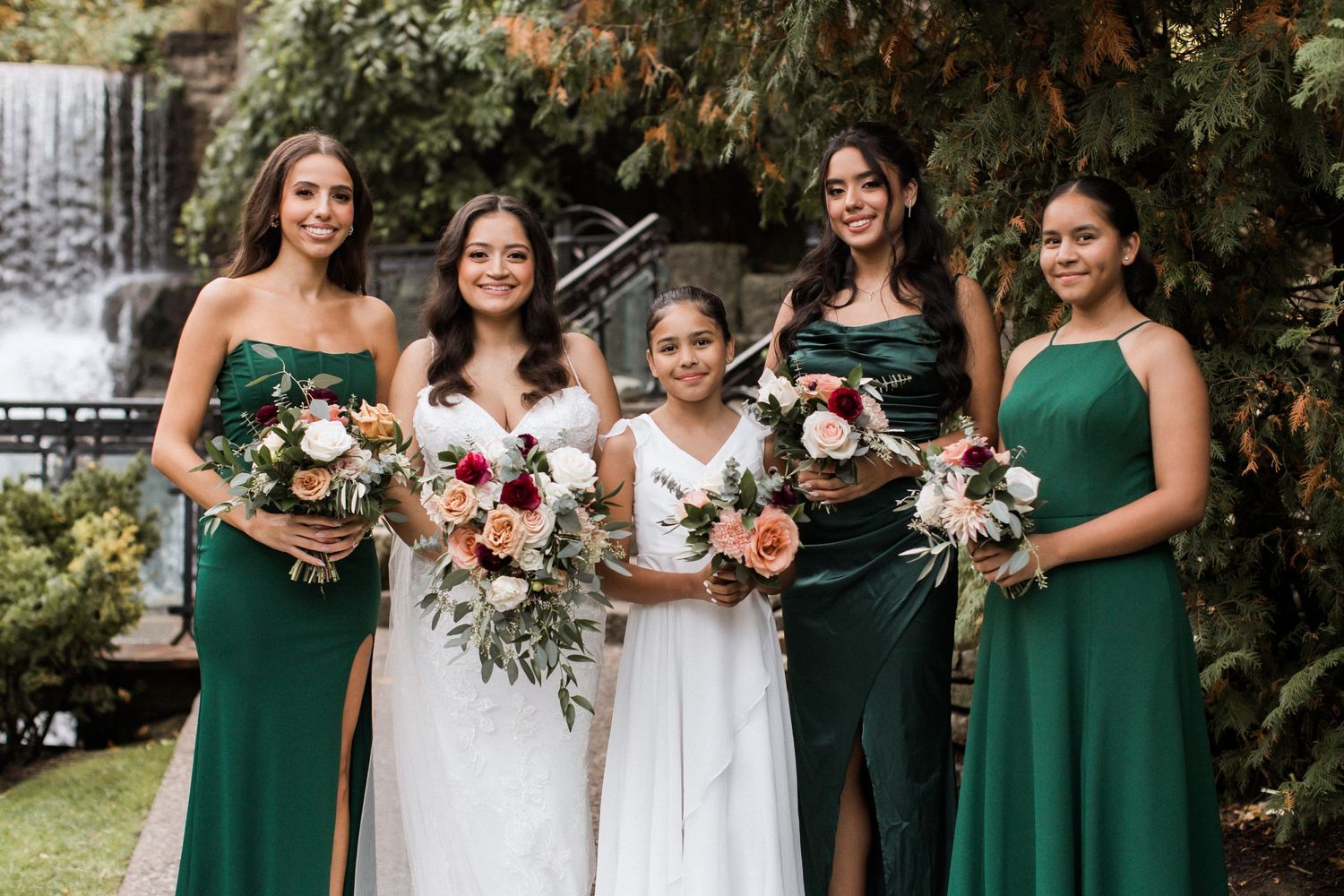 Bridal party members wearing green dresses hold bouquets of pink and white flowers.