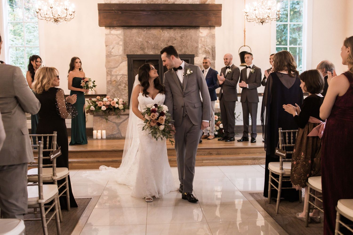 Beautiful wedding recessional in an elegant white room with stone fireplace and crystal chandeliers.