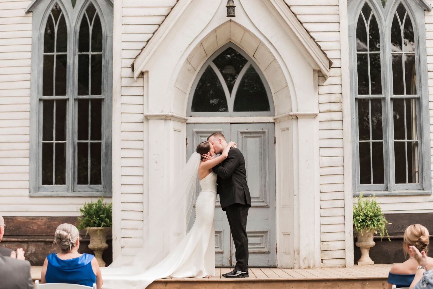 A romantic moment between newlyweds at a classic white church with gothic arched windows and doorway.