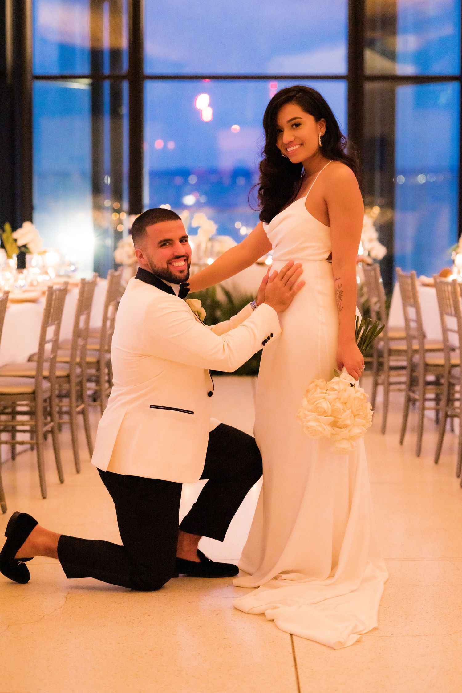 Romantic moment captured in elegant reception venue with city lights in background.