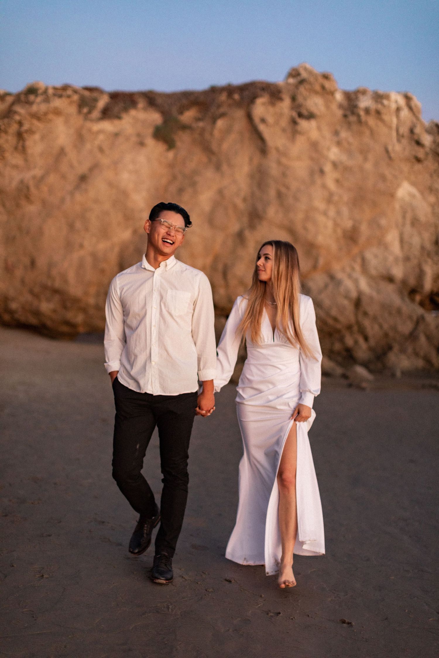 Couple sharing joyful moment while walking near coastal cliffs at sunset.