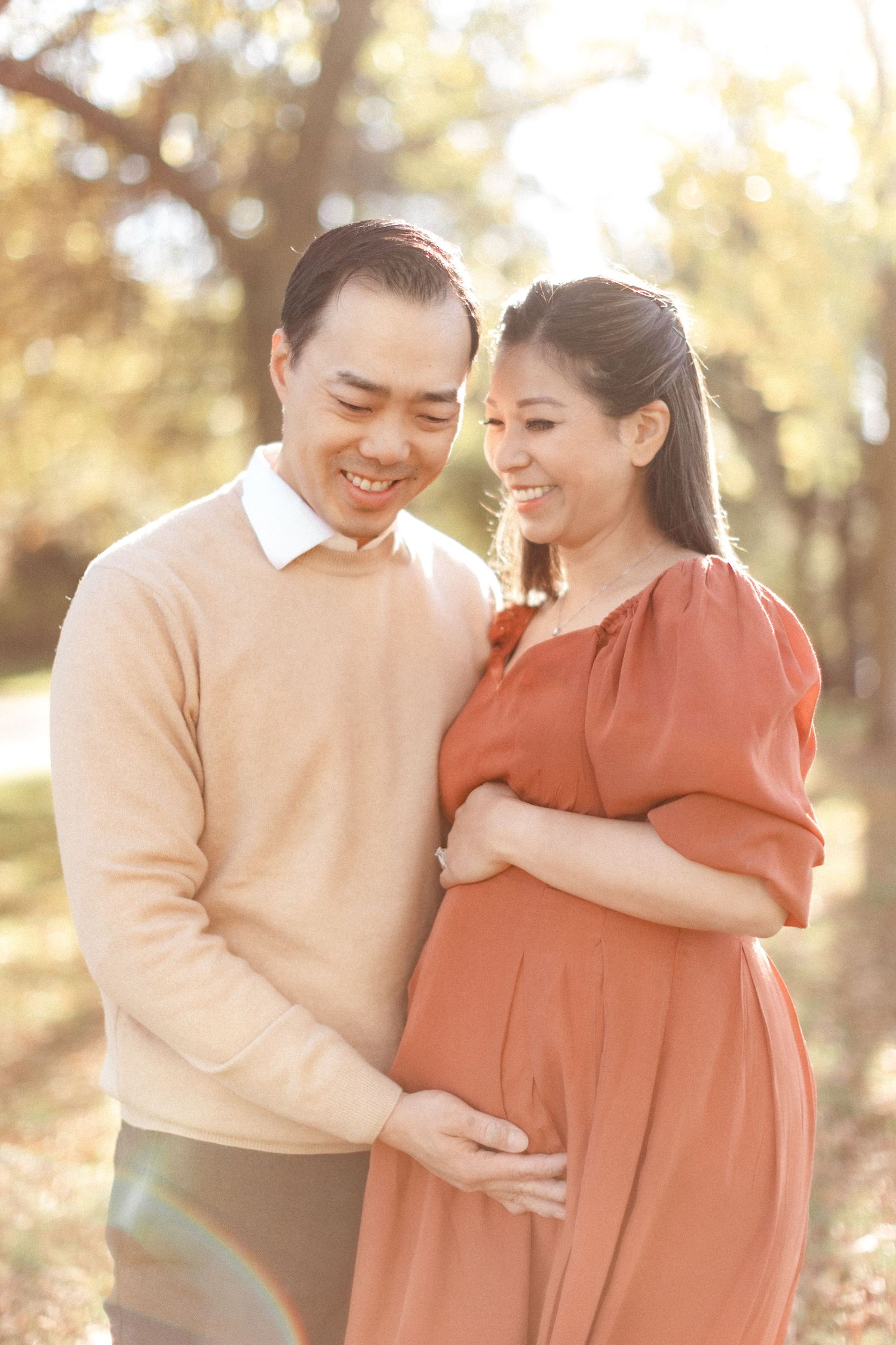 Expectant couple sharing tender moment in golden sunlight during outdoor maternity session.