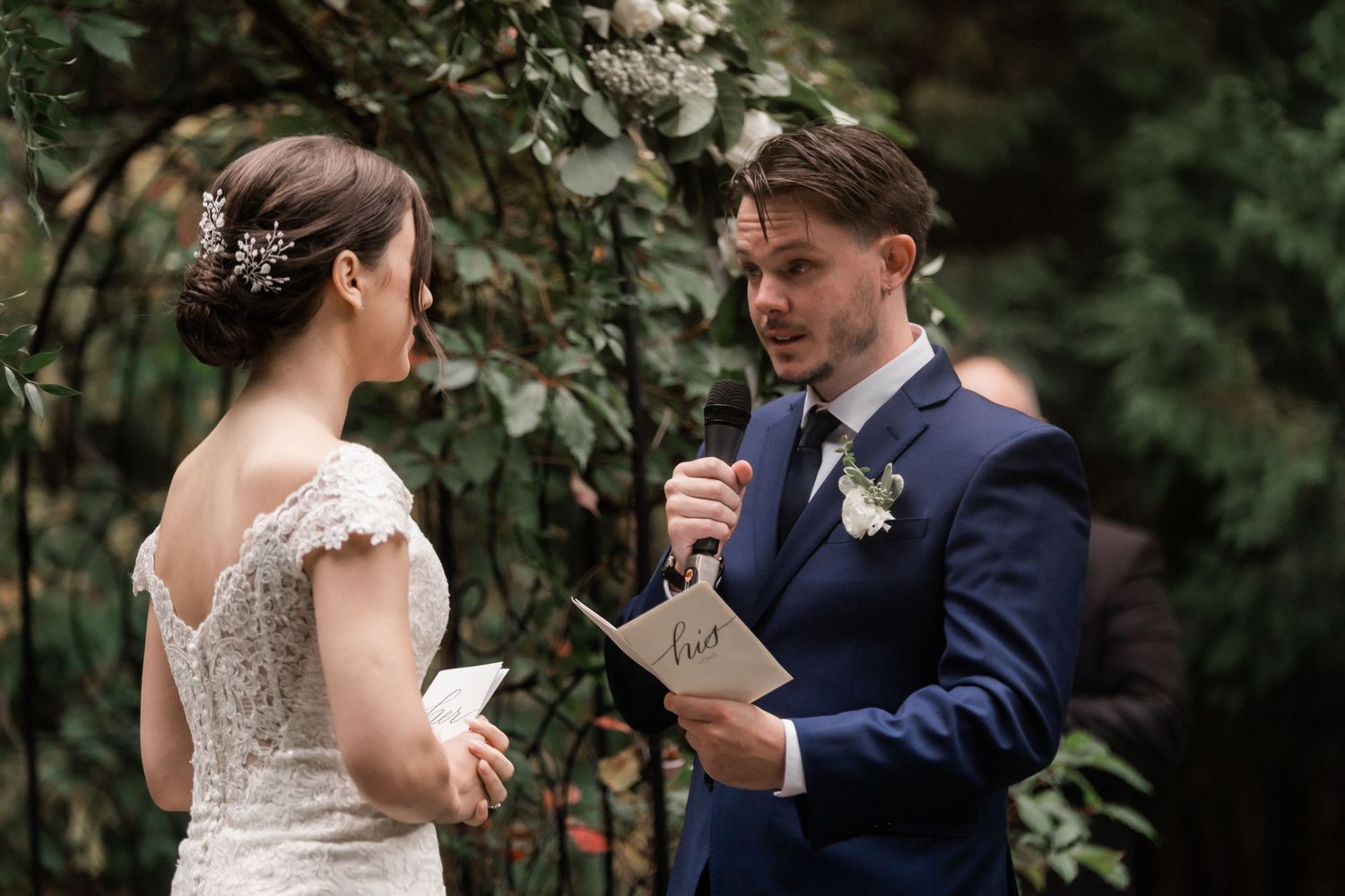A couple exchanges personal vows under a floral-adorned garden arch.