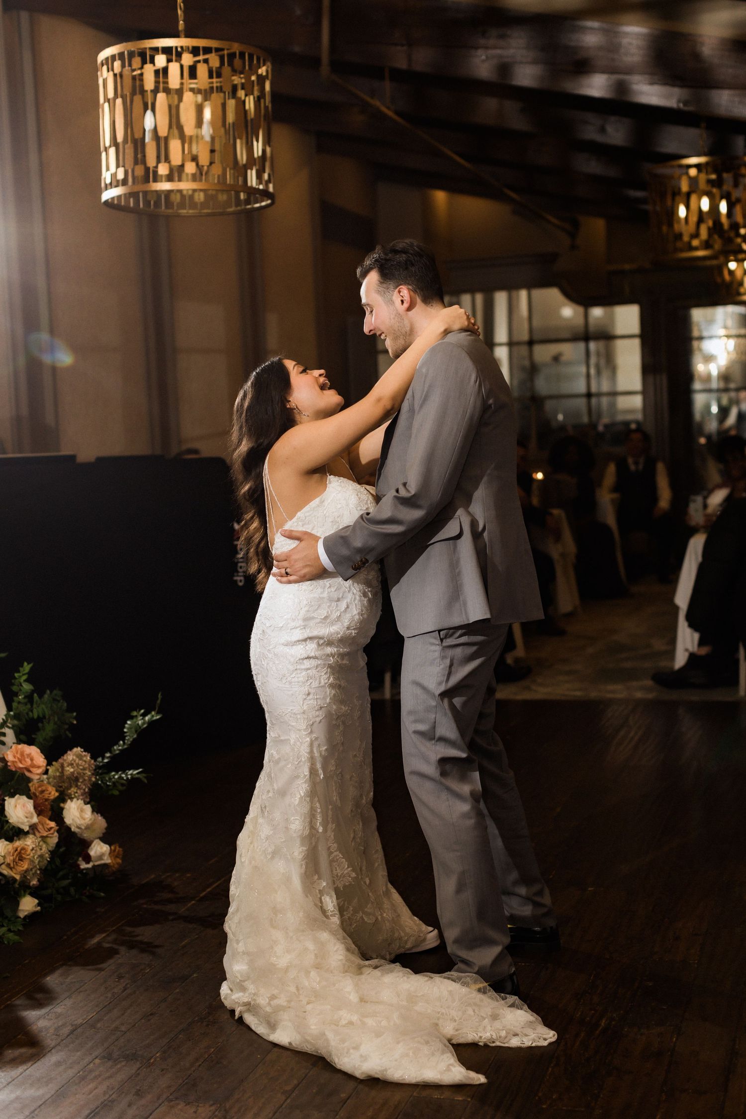 A couple embraces during their wedding dance under decorative gold pendant lights.