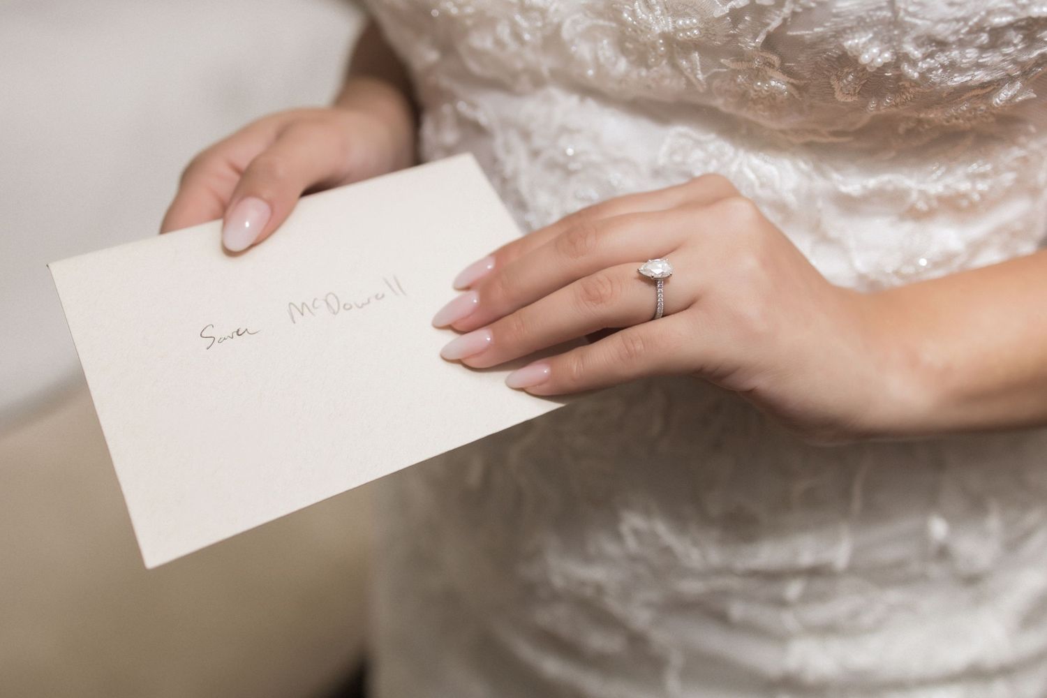 Close-up of bride's hands holding a white letter or note while wearing her wedding dress.
