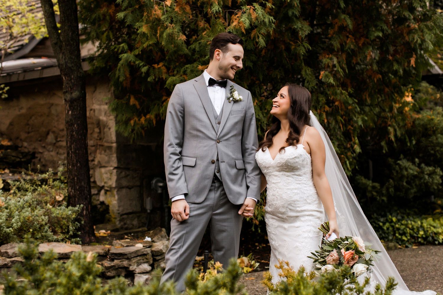 Newlywed couple shares joyful moment in autumn garden with waterfall backdrop.