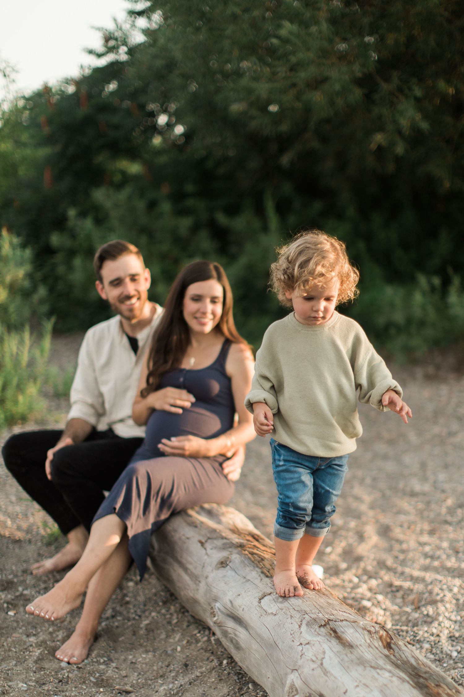 Family relaxes together on a driftwood log at the beach during a warm summer evening.