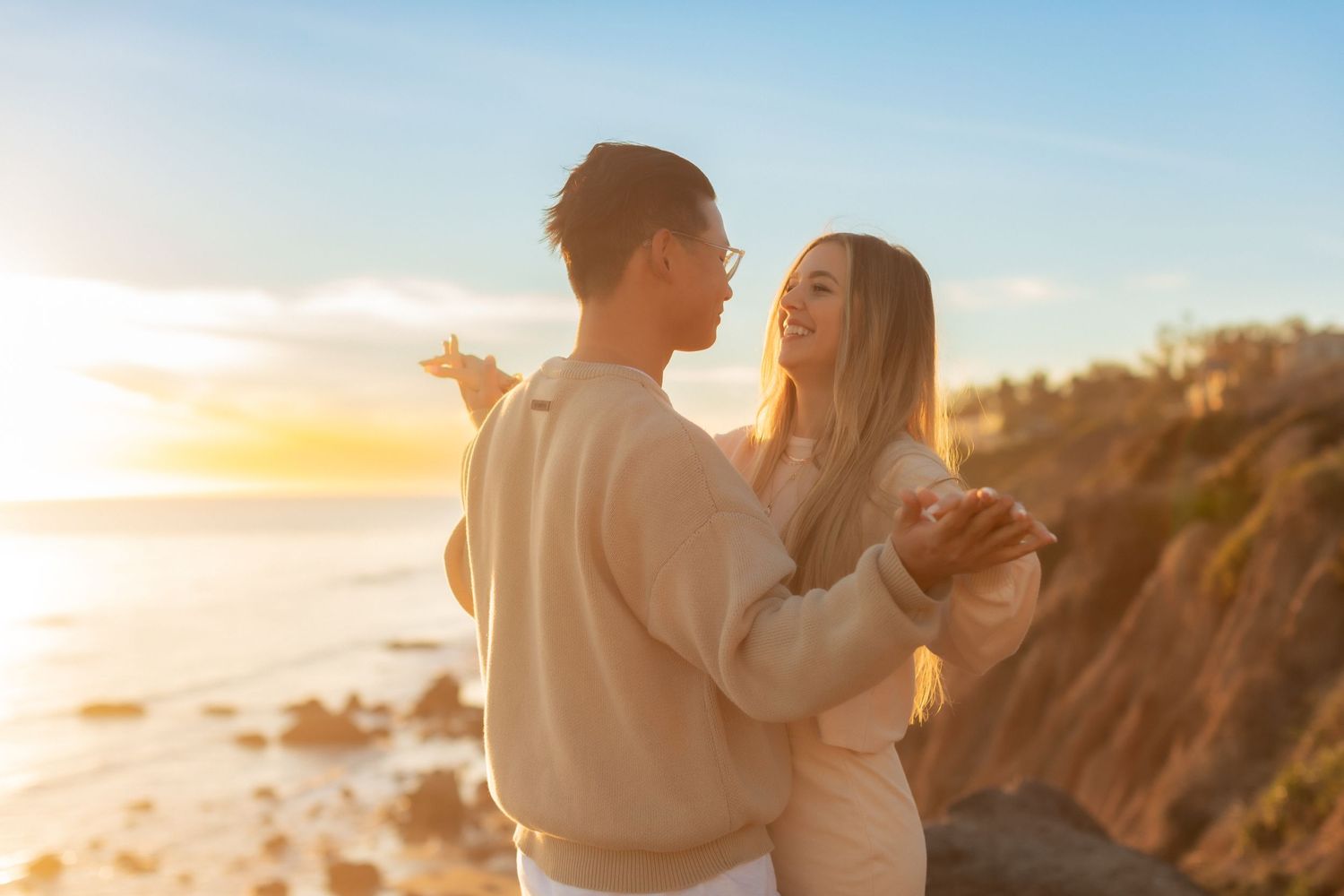 Two people embrace during golden hour sunset at a scenic coastal cliffside overlook.