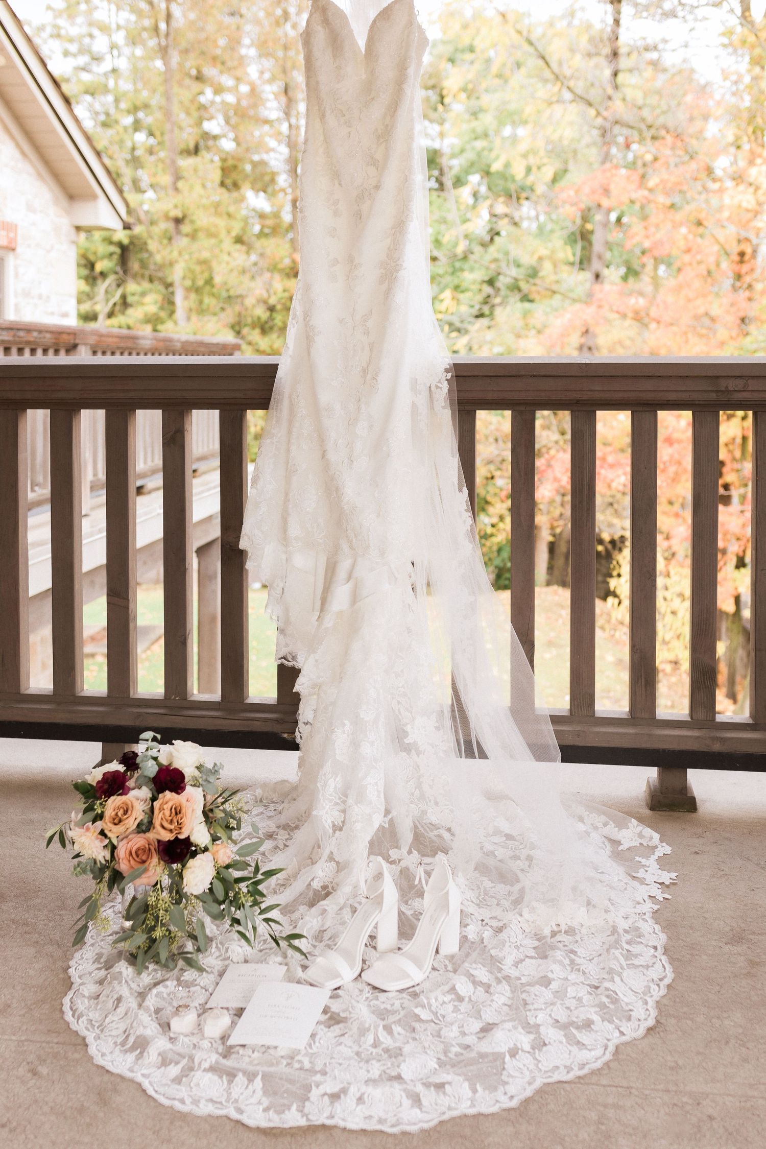 White lace wedding gown displayed on porch with trailing train and floral bouquet at base.