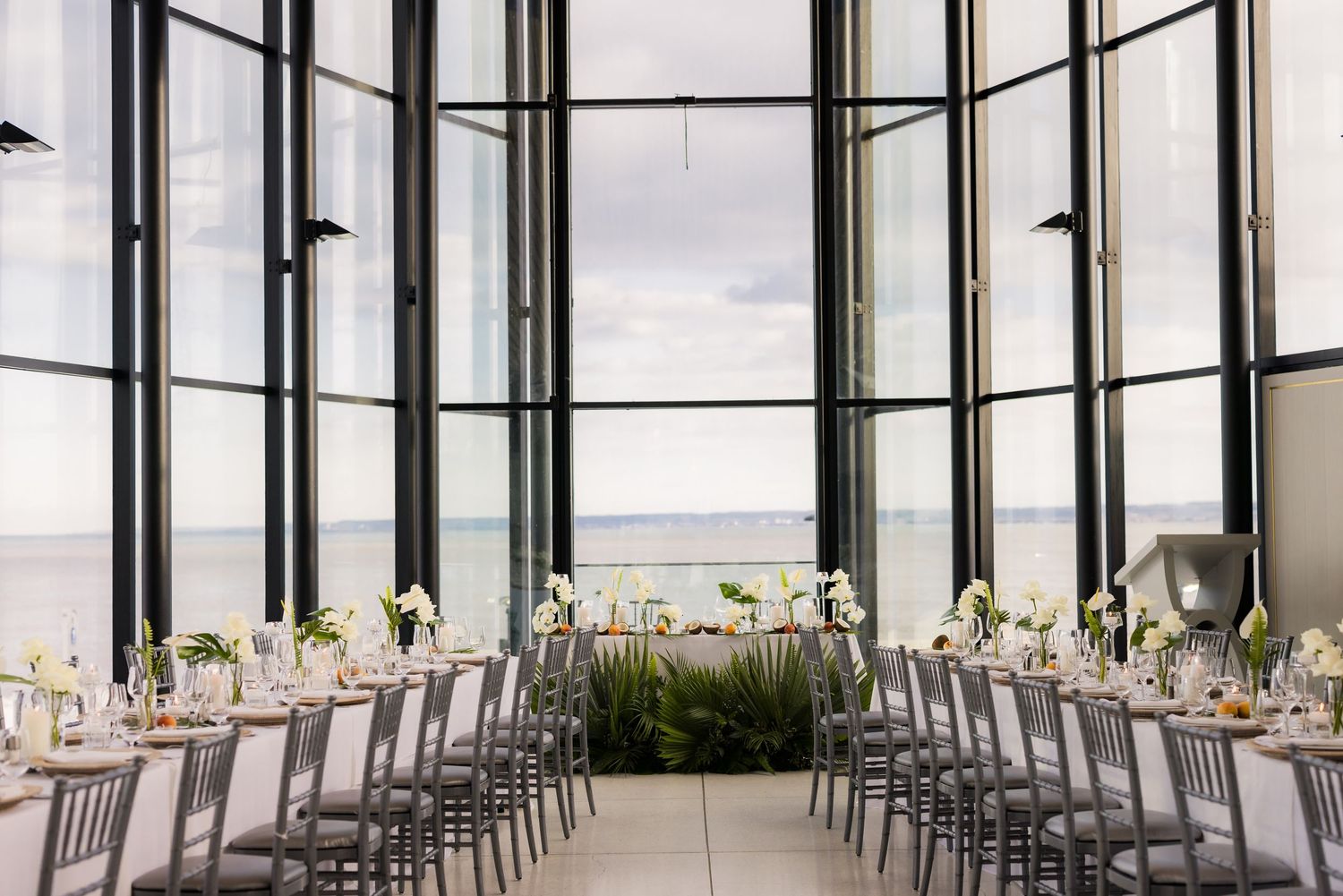 Modern reception hall with panoramic windows and long dining tables set with elegant place settings.