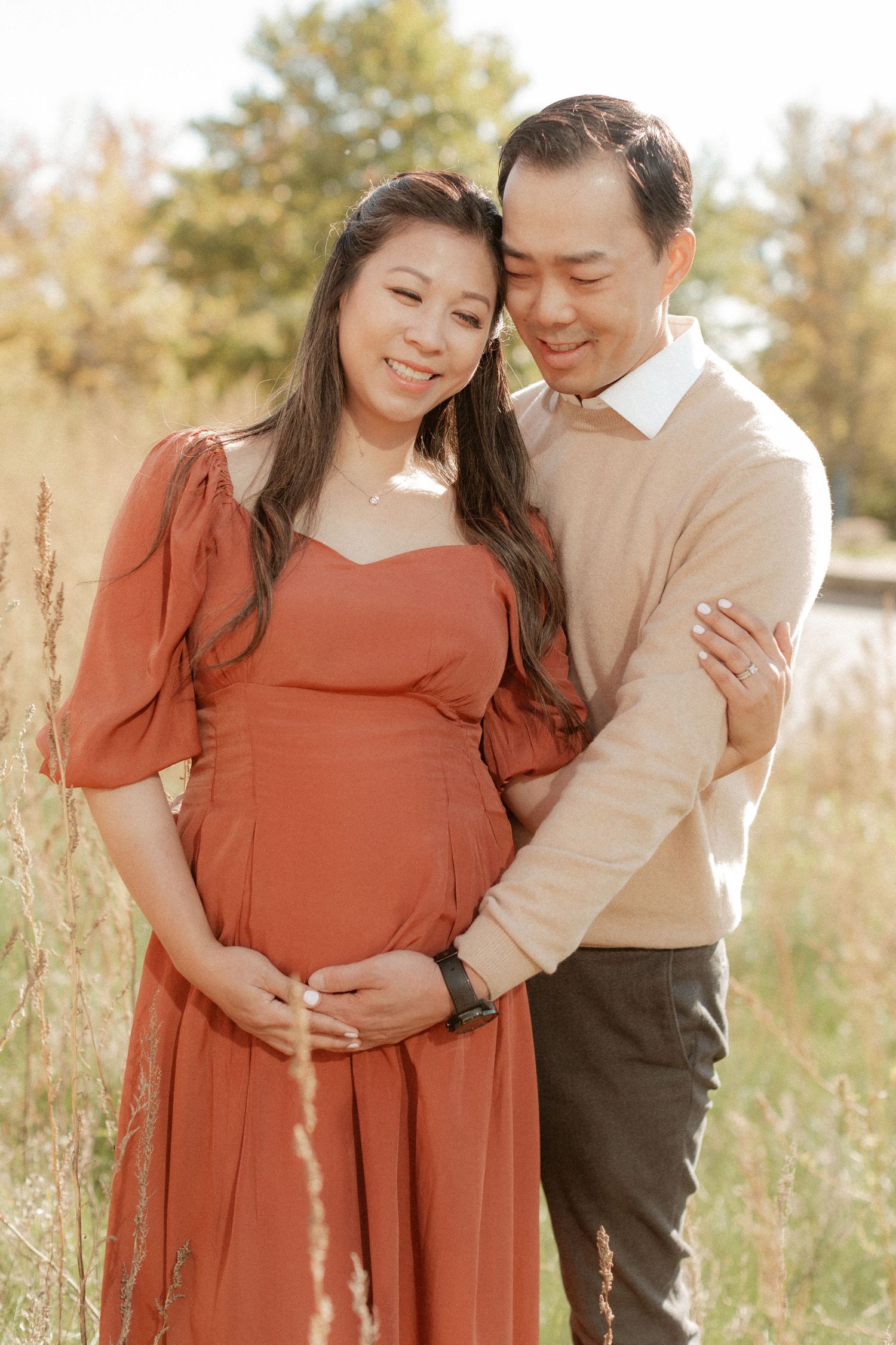 A joyful maternity portrait captured in warm natural lighting among tall grasses.