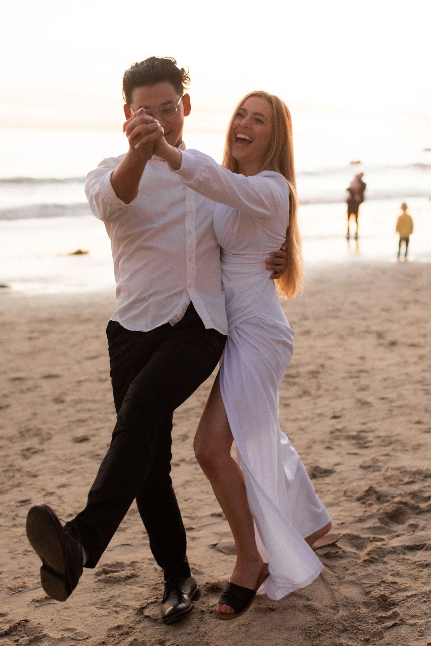 Joyful couple dancing energetically on the beach with scenic ocean backdrop.