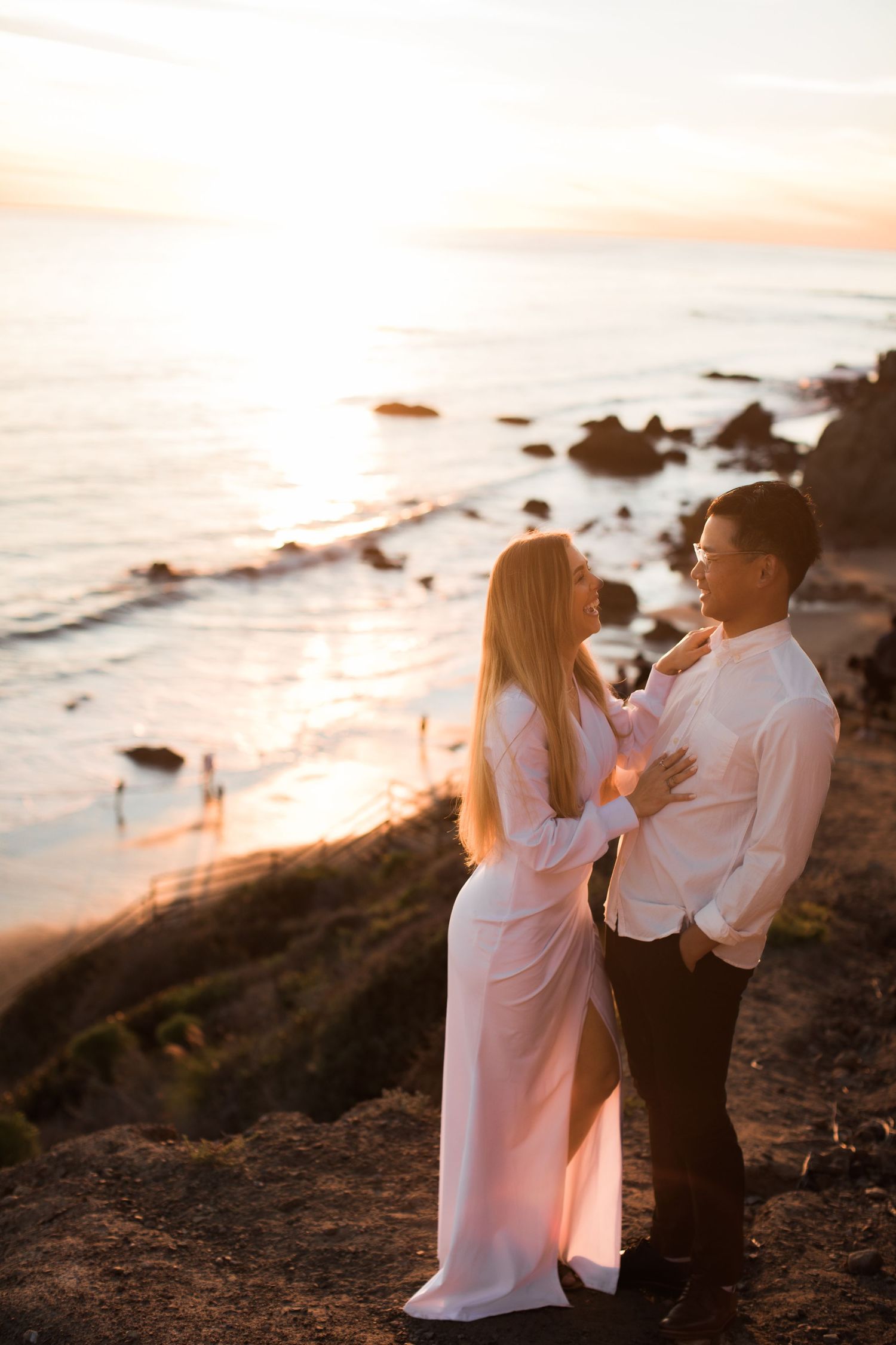 Romantic couple embraces on coastal cliffs during golden hour sunset over the ocean.