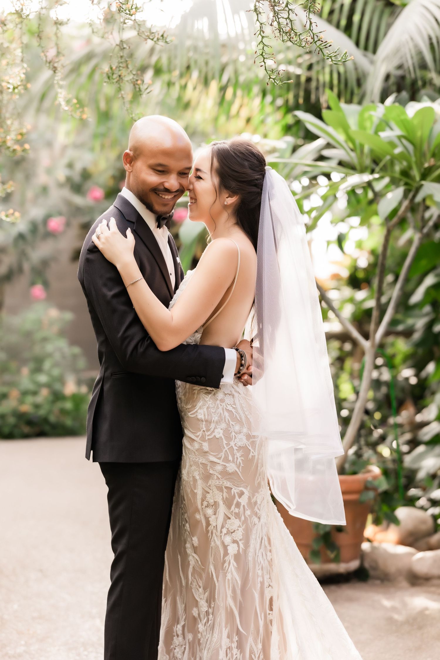 Joyful wedding couple laughing together in a beautiful greenhouse setting.