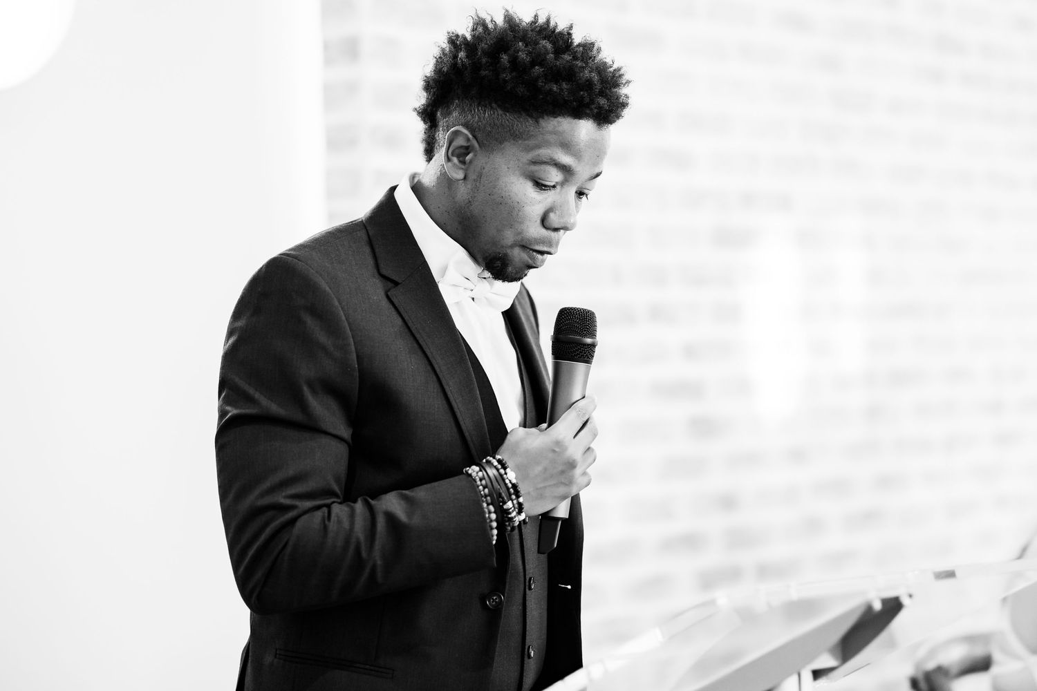 A speaker in a black suit delivers an emotional speech at a wedding reception.