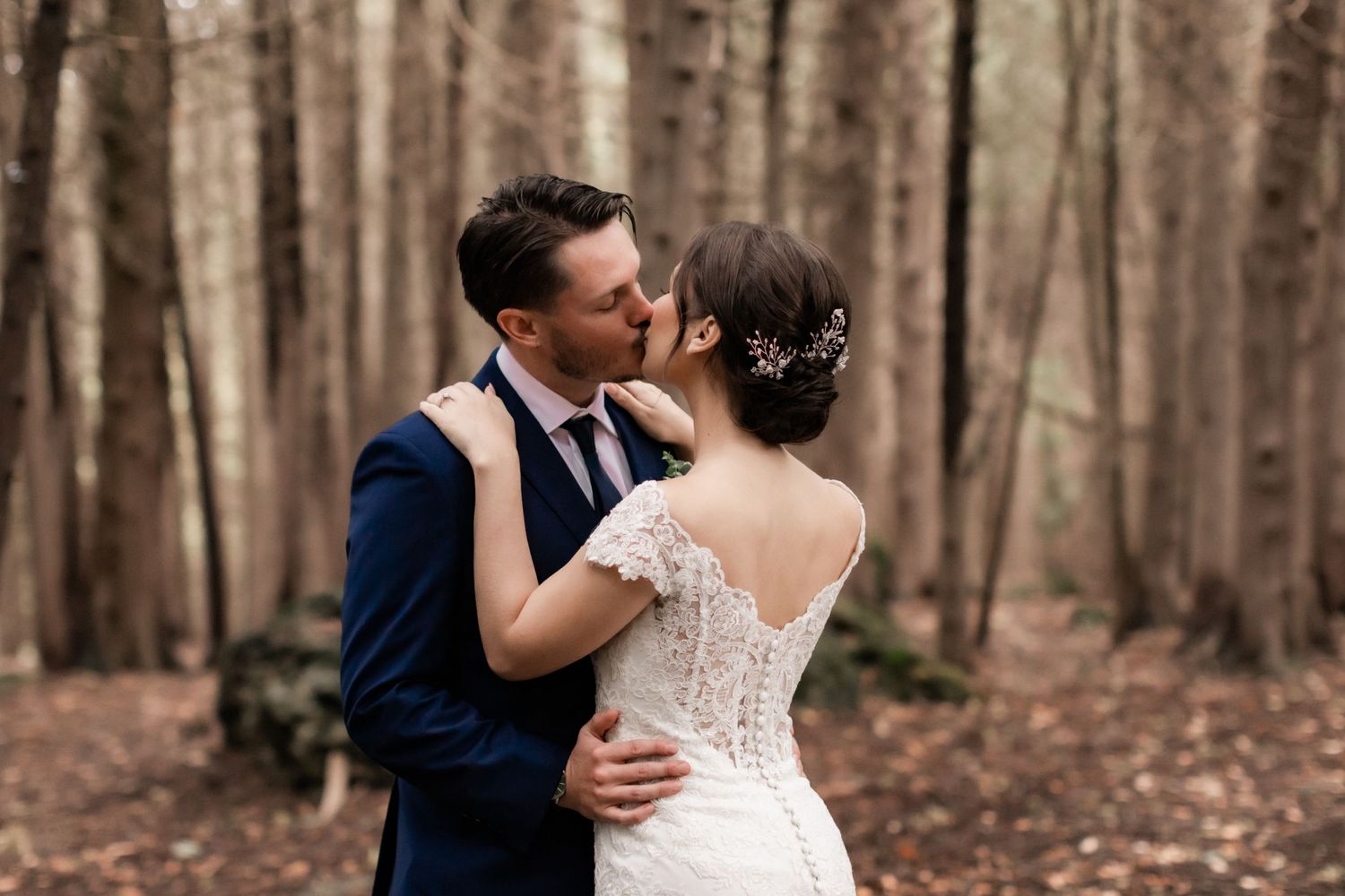 Romantic moment between newlyweds with detailed lace back dress in forest setting.