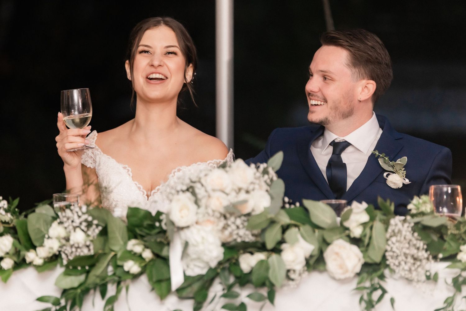 Wedding couple smiling at reception while toasting with wine glasses.