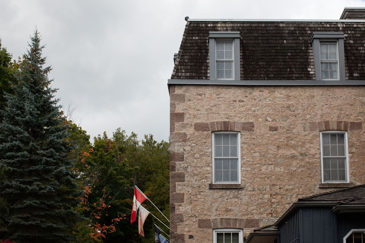 Stone mansion exterior with mansard roof and windows against cloudy sky.