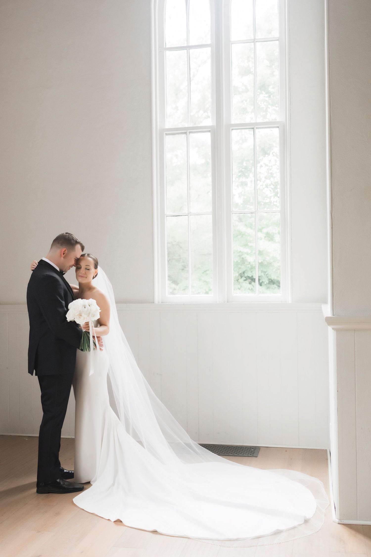Romantic wedding photo series showing a bride and groom sharing intimate moments in a bright white minimalist room.