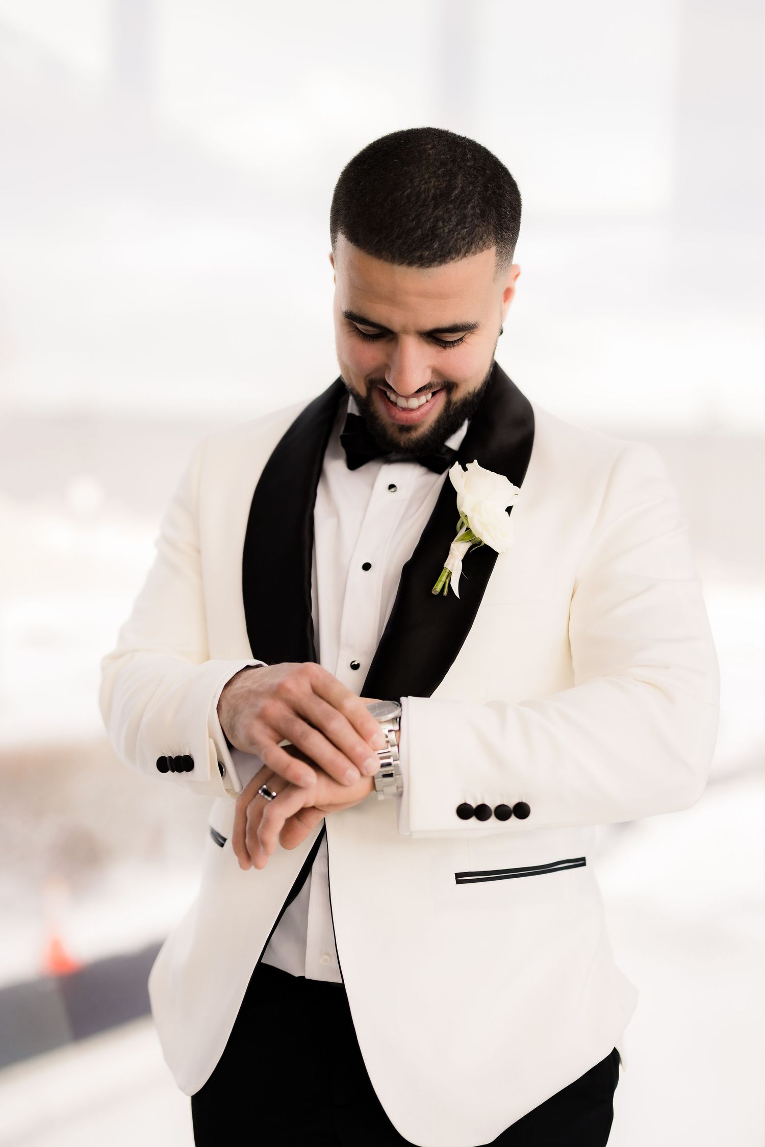 Groom in white tuxedo jacket adjusts cufflinks during wedding photoshoot.