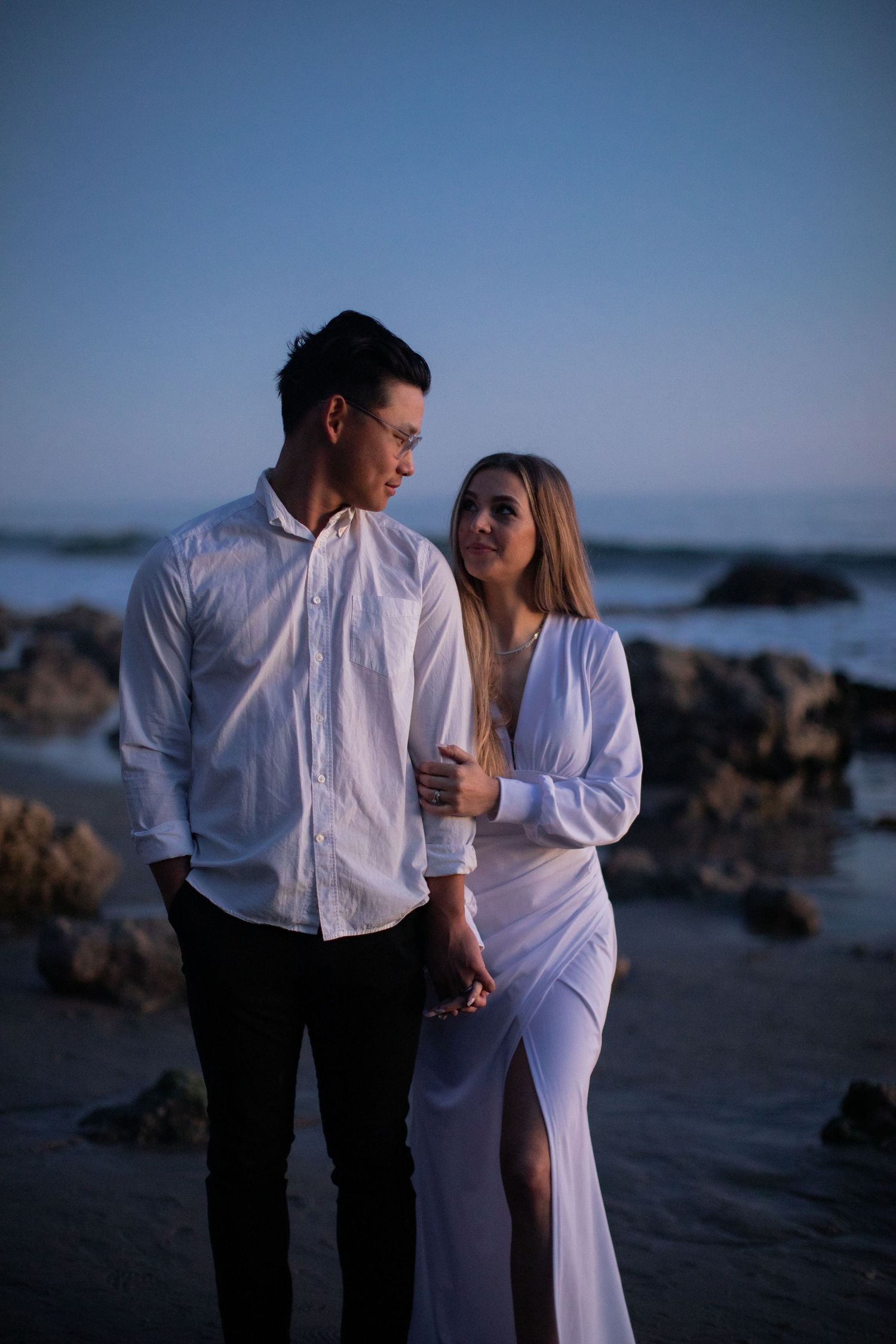 Intimate beachside portrait of couple in white clothing during blue hour.