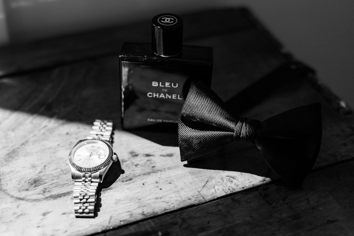 Black and white photo of a bowtie, watch and Chanel Bleu cologne on marble surface.
