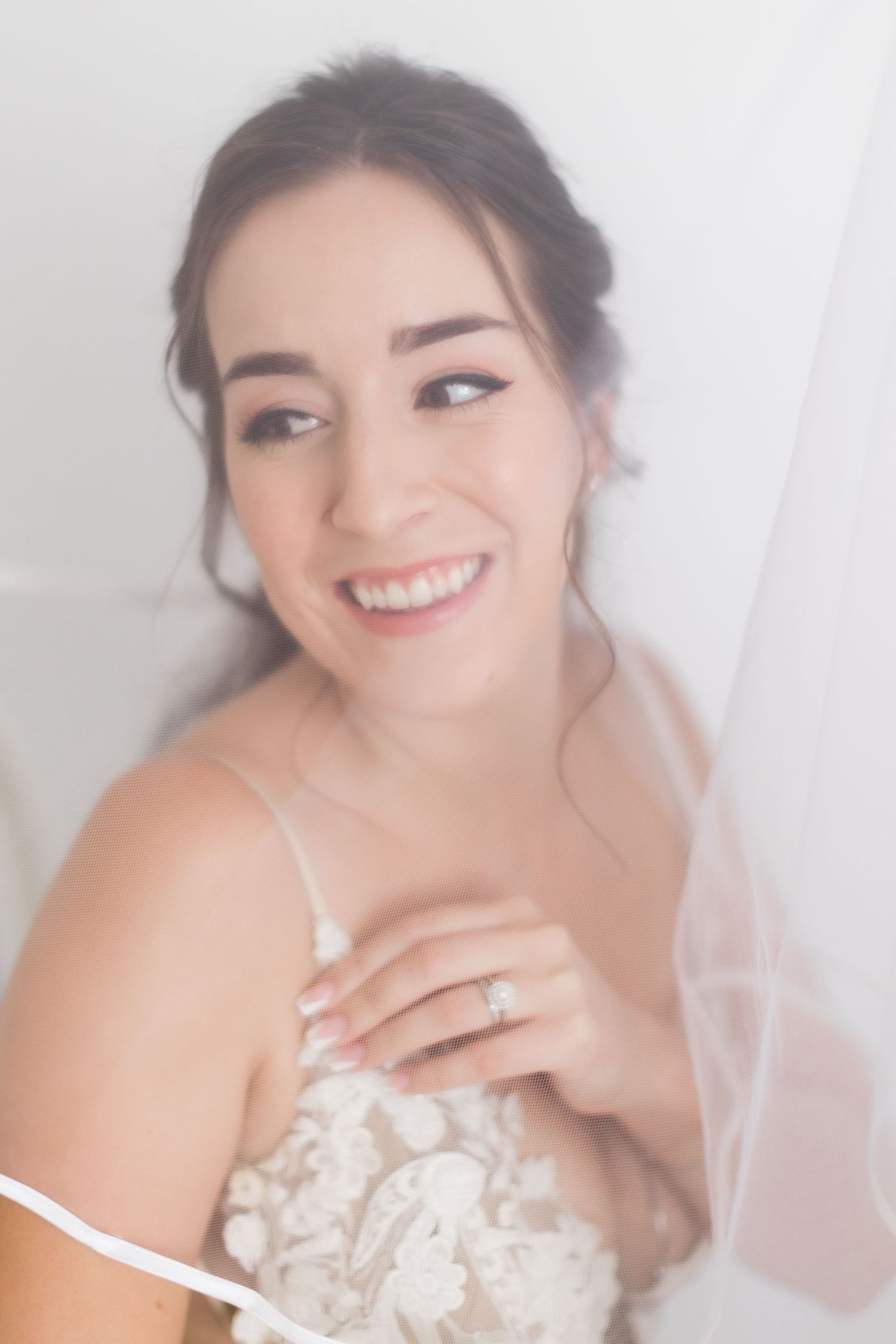Dreamy bridal portrait through veil showing radiant smile and lace wedding dress.