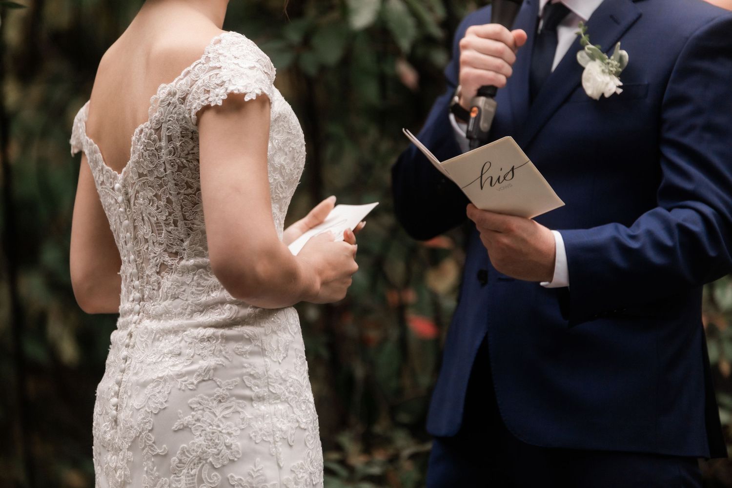 Close-up of couple holding ceremony papers while exchanging vows at garden wedding.