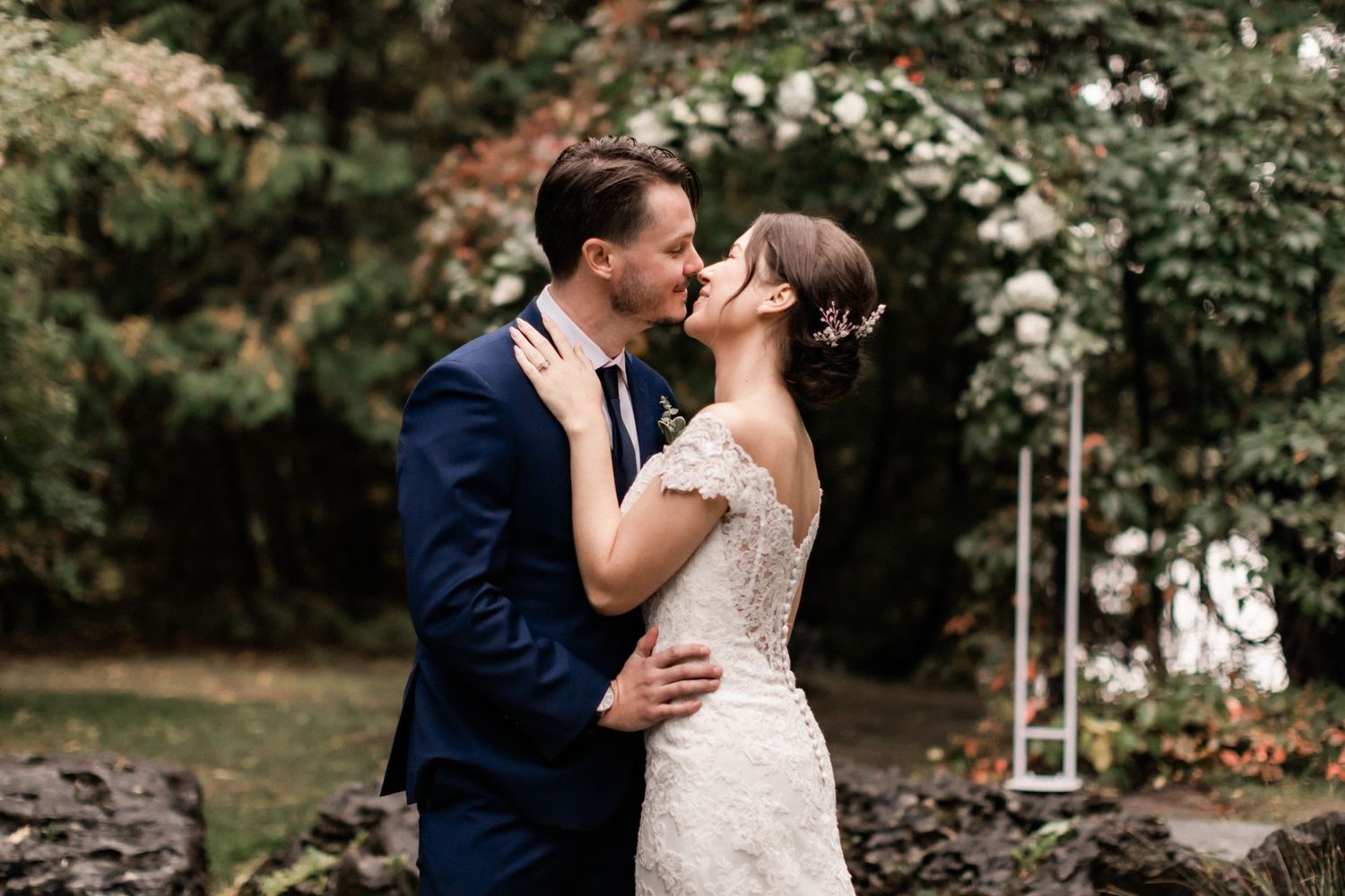 Romantic wedding couple sharing a kiss in a garden setting with a rustic stone wall backdrop.
