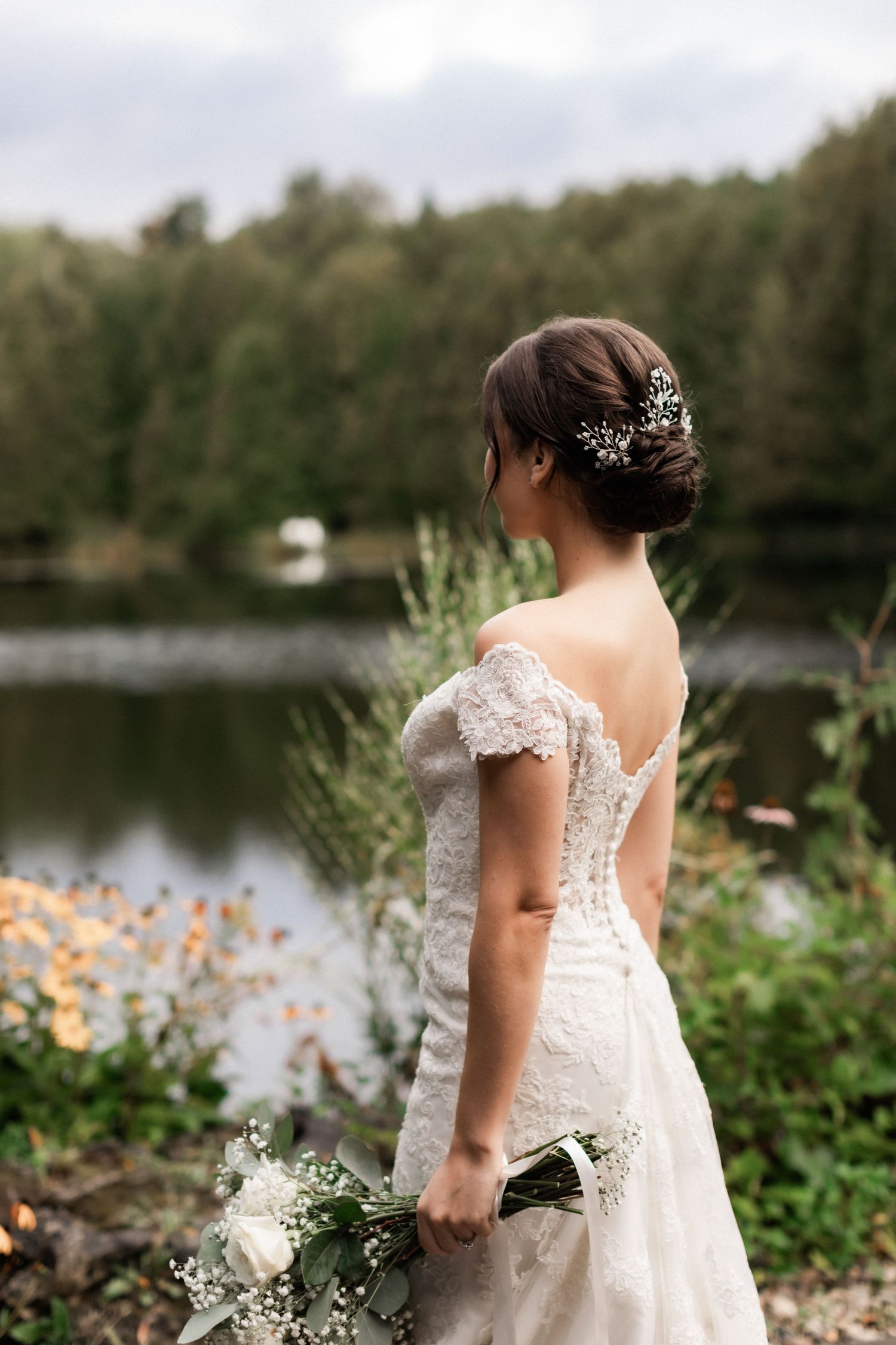 A lace wedding dress with delicate back detail is captured against a lakeside backdrop.
