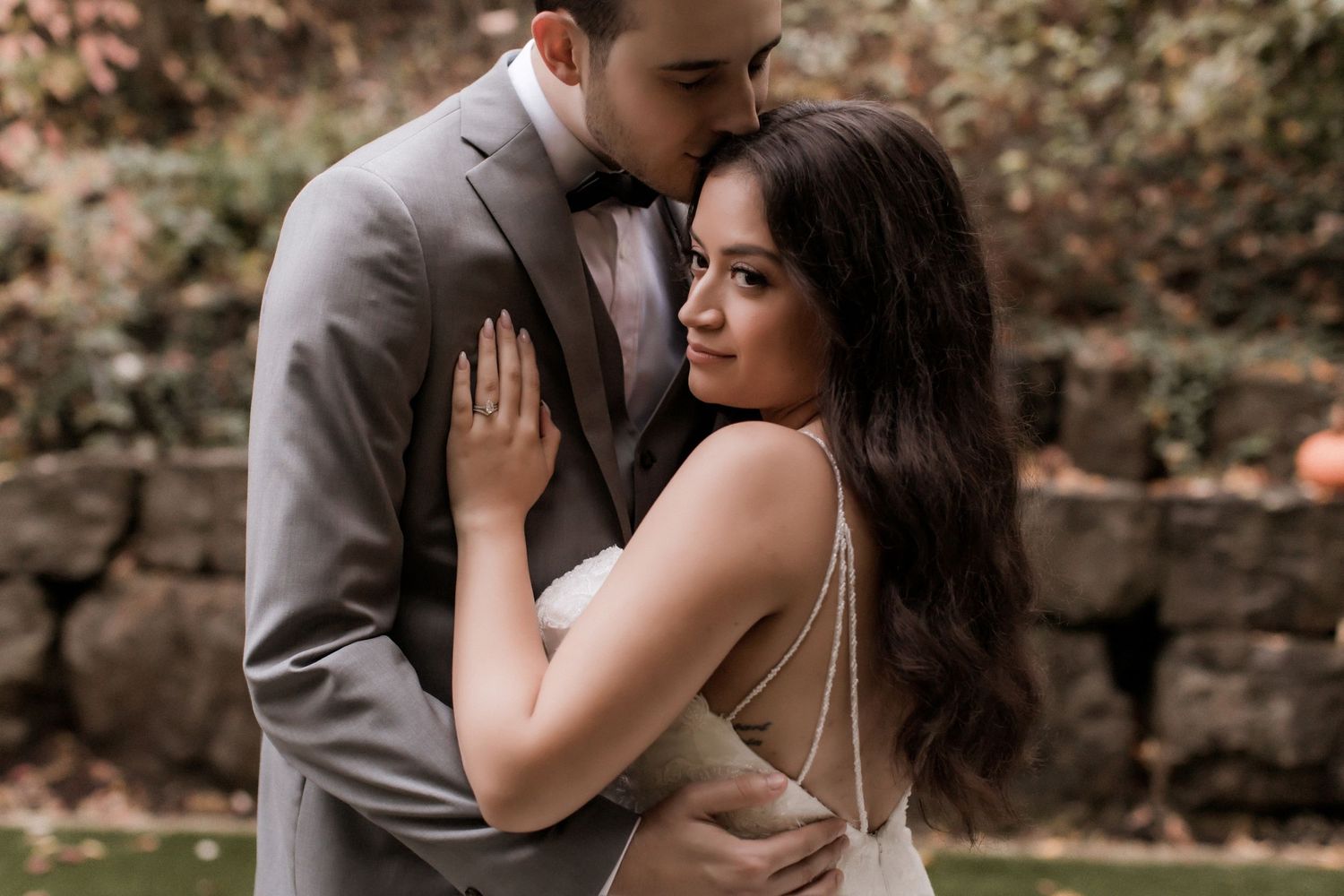 Romantic wedding couple embraces outdoors in an intimate portrait against a stone wall background.
